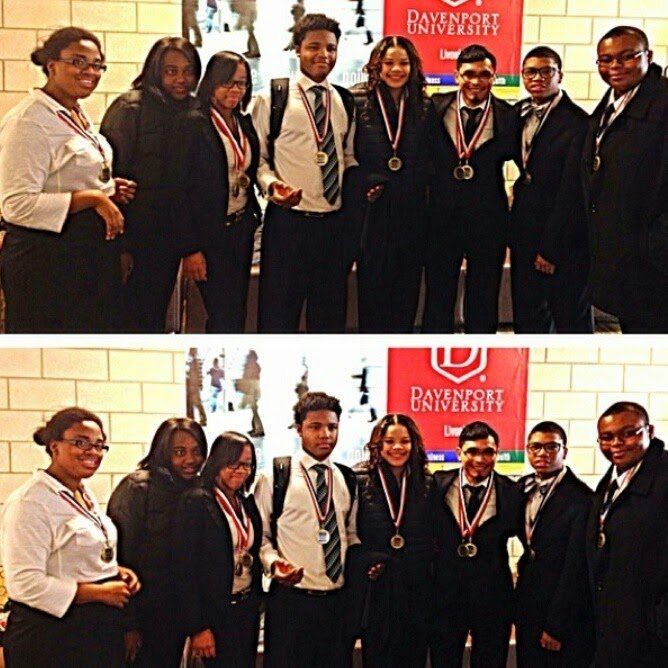 A group of eight young adults wearing conference badges and medals standing in front of a Davenport University sign at an event or conference.