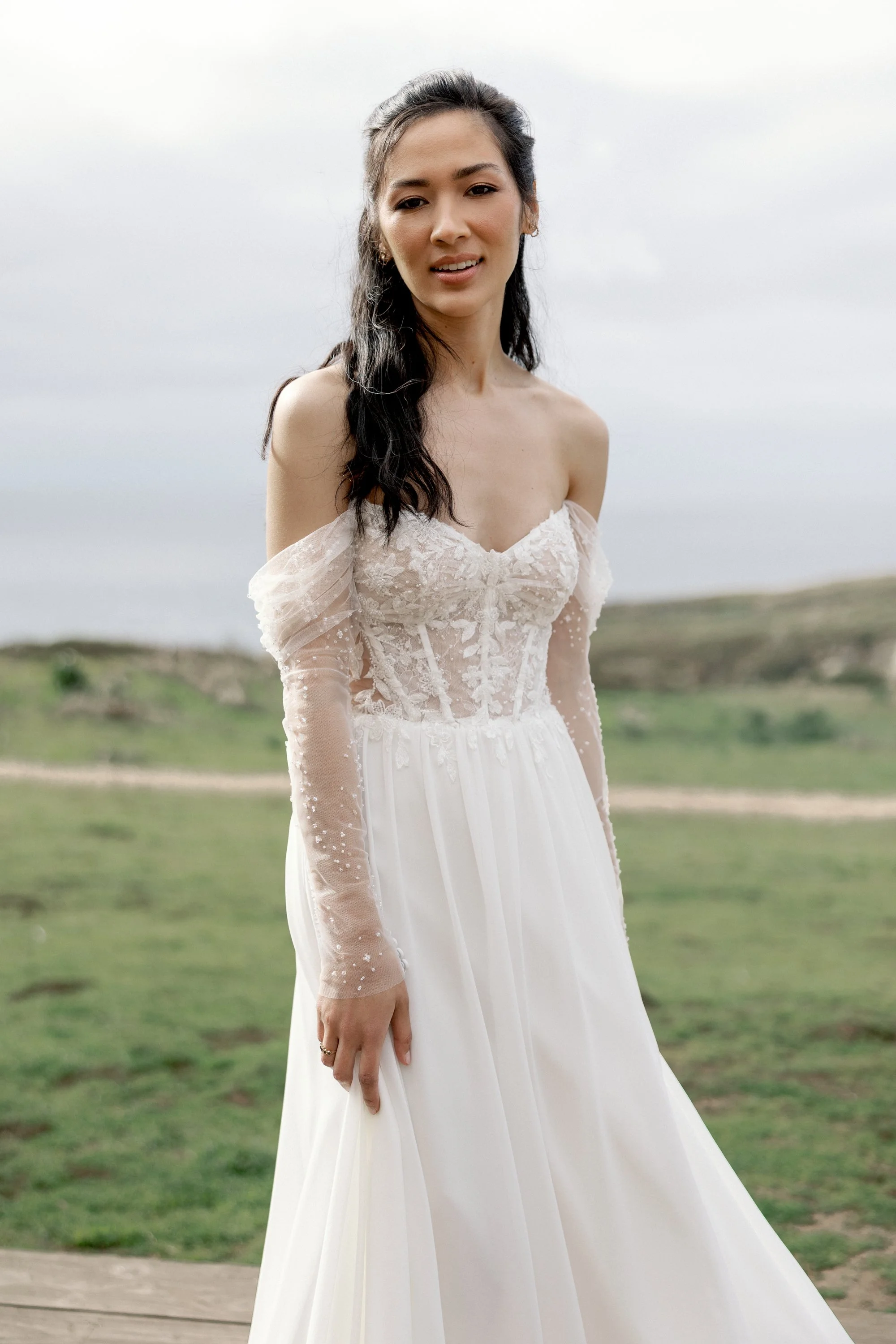 A woman in a strapless white wedding dress outdoors on a cloudy day.