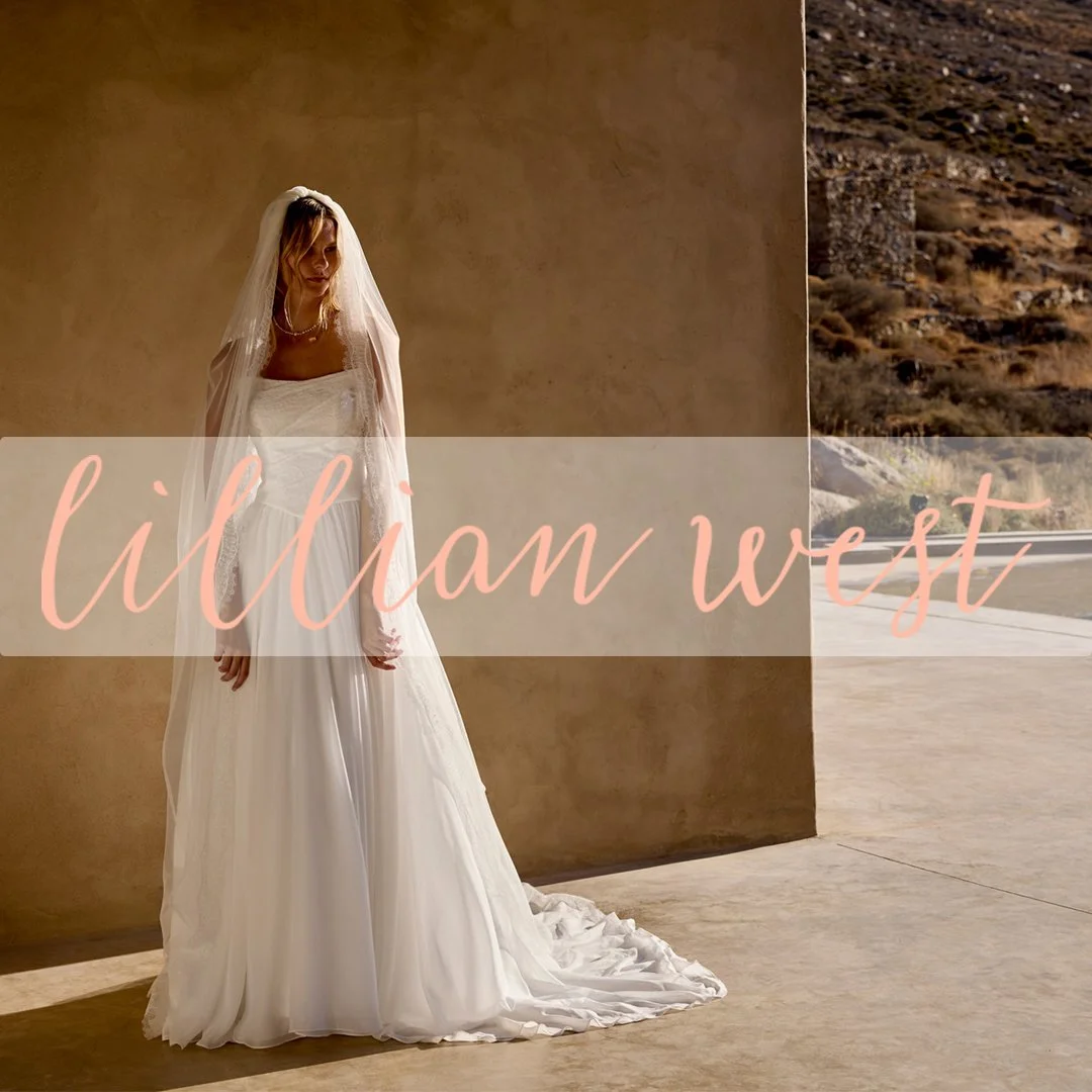 A woman in a wedding dress with a veil standing indoors beside a tan wall, with a view of a desert landscape through an open doorway. The logo 'Lillian West' is overlaid on the image.