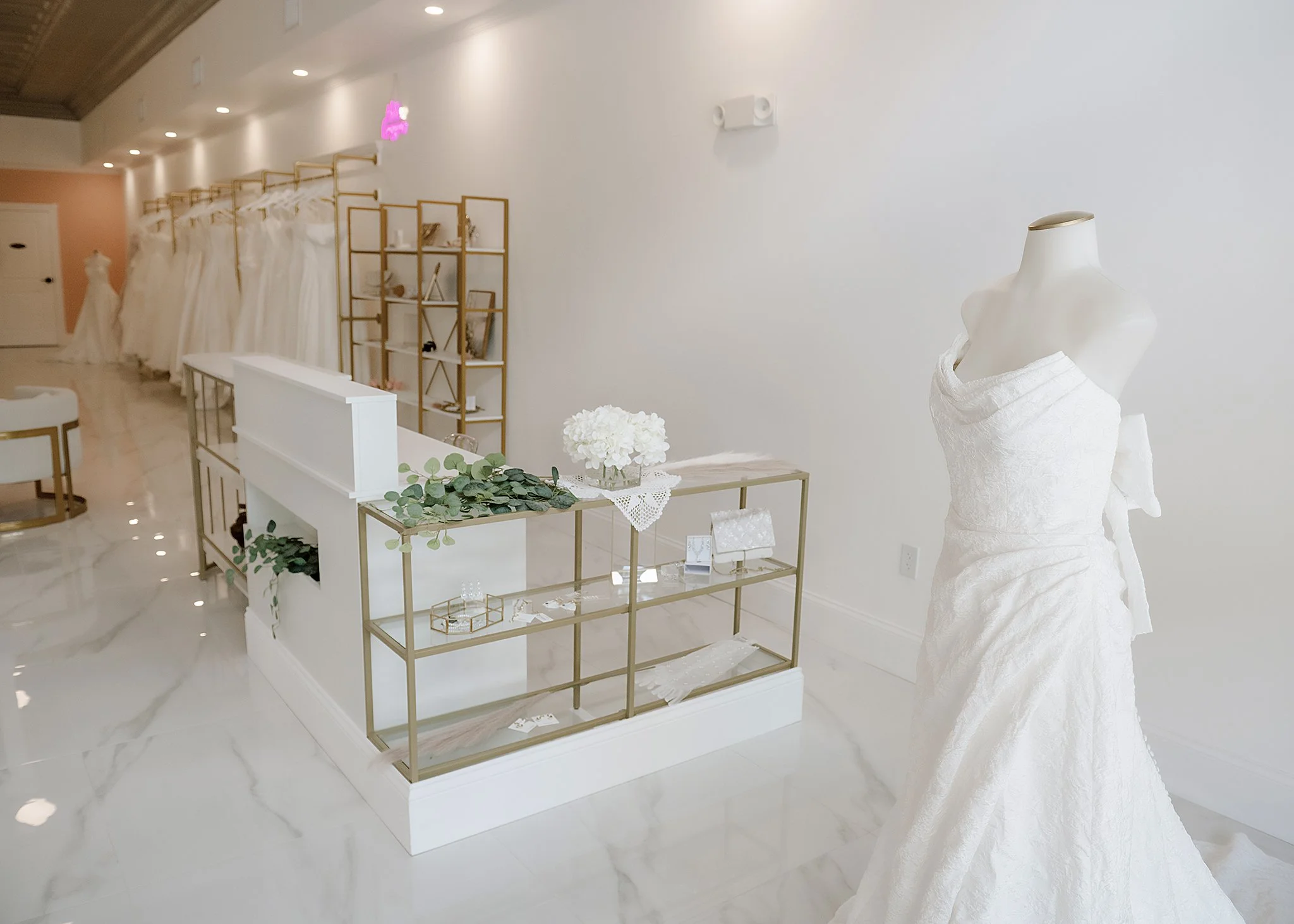 Beautiful bright white interior of the Luxe Bride Boutique in downtown Lake Wales, Florida. Wedding dresses are hanging on the walls. Checkout counter and a wedding dress on a mannequin  are in the foreground.