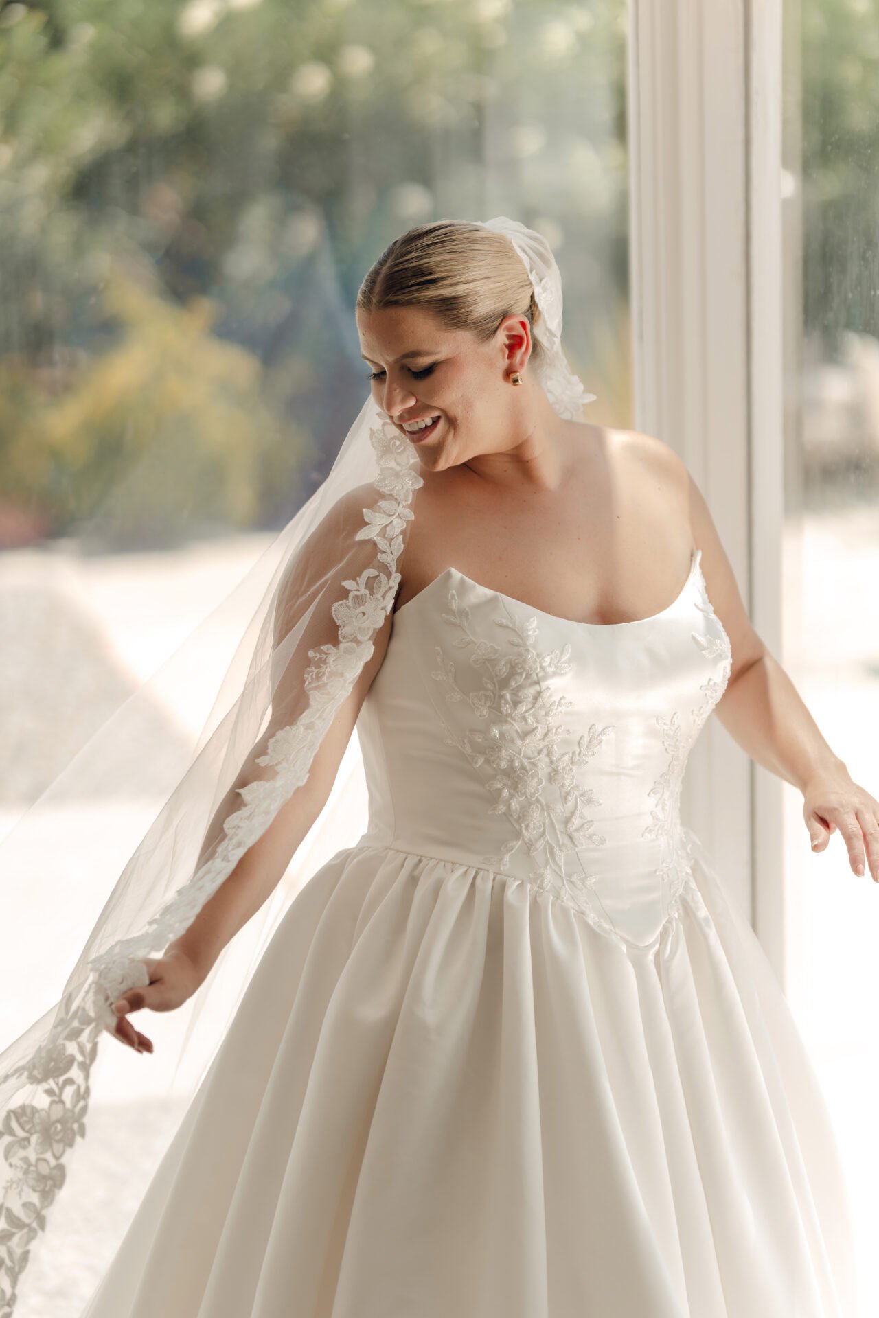 Stella York basque waist satin ball gown with cat eye swoop neckline and beaded appliques on the bodice. Long cathedral lace trimmed veil.