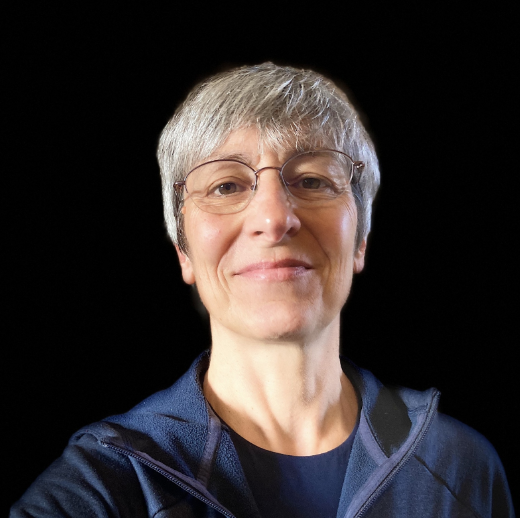 A person with short gray hair, glasses, and a black shirt standing in front of a wooden wall with a city skyline visible in the background.