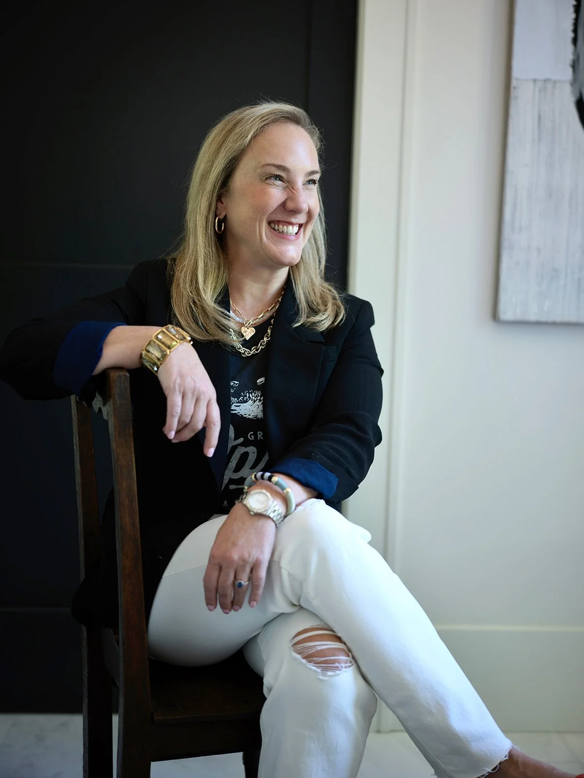 Kristen Mills smiling in a black blazer, wearing gold jewelry, seated indoors with a dark background and a window to her right. IDS member spotlight image