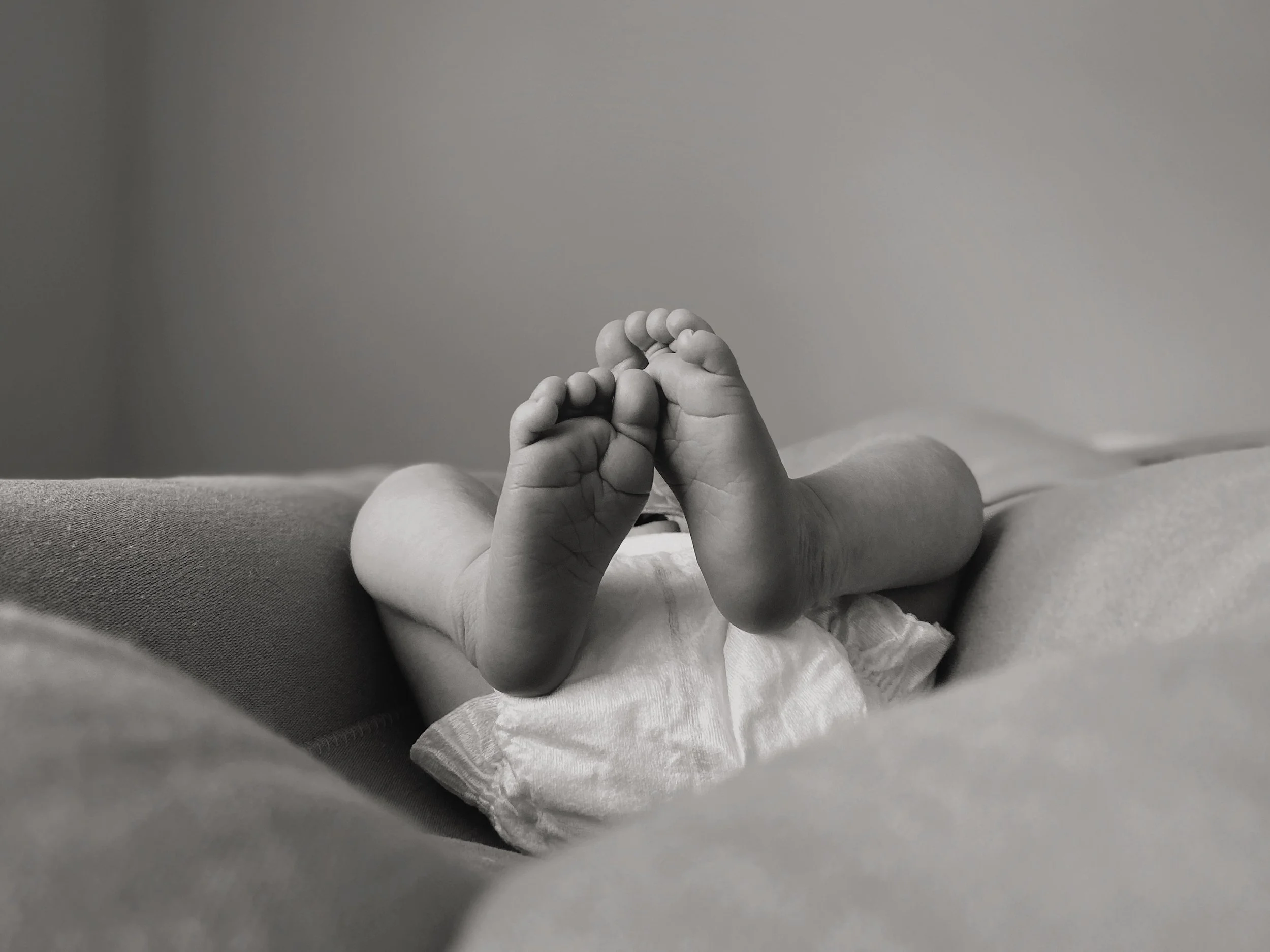 Newborn baby feet resting on soft fabric, photographed in black and white.
