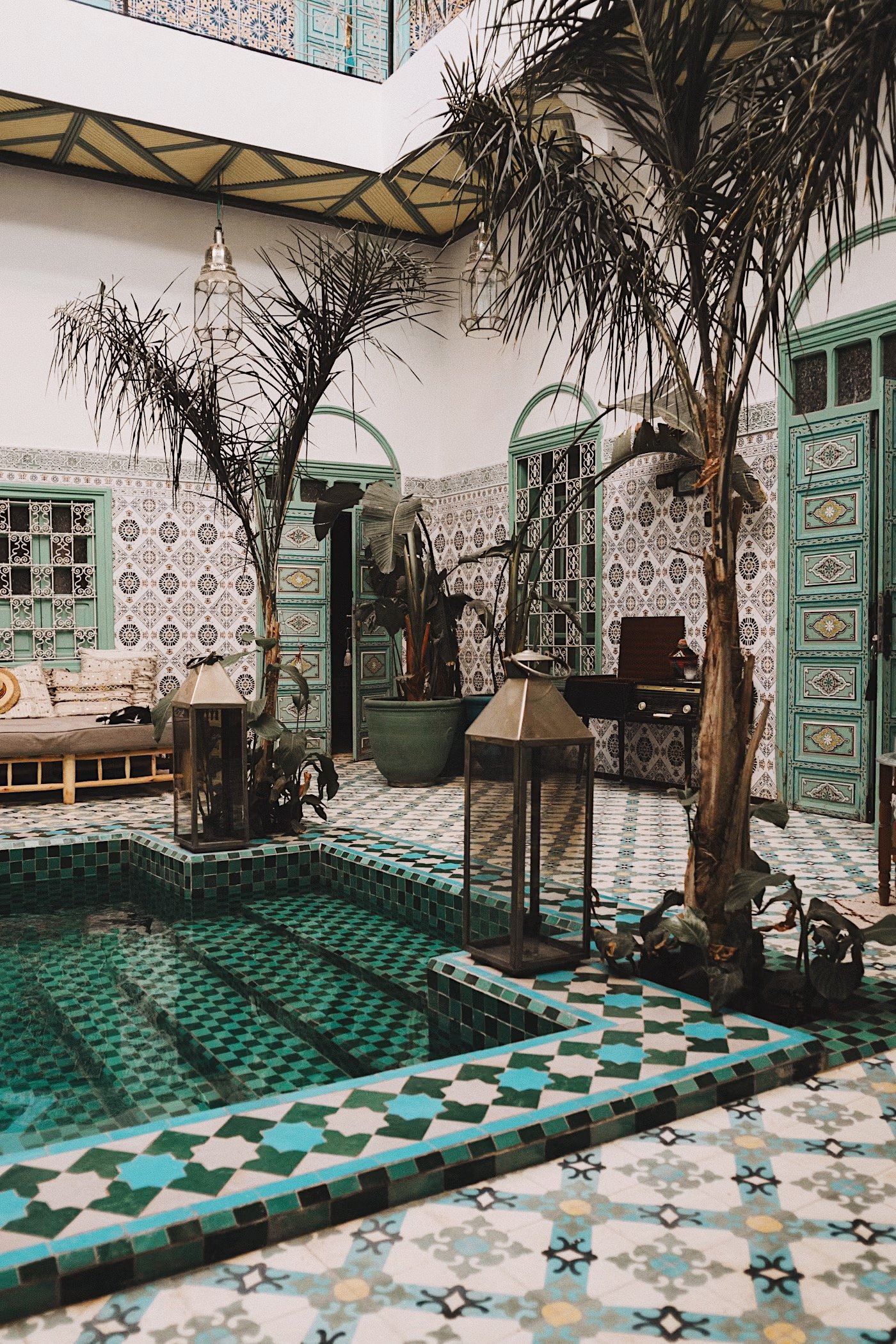 Tiled courtyard with a shallow pool and palm trees inside a Marrakech riad