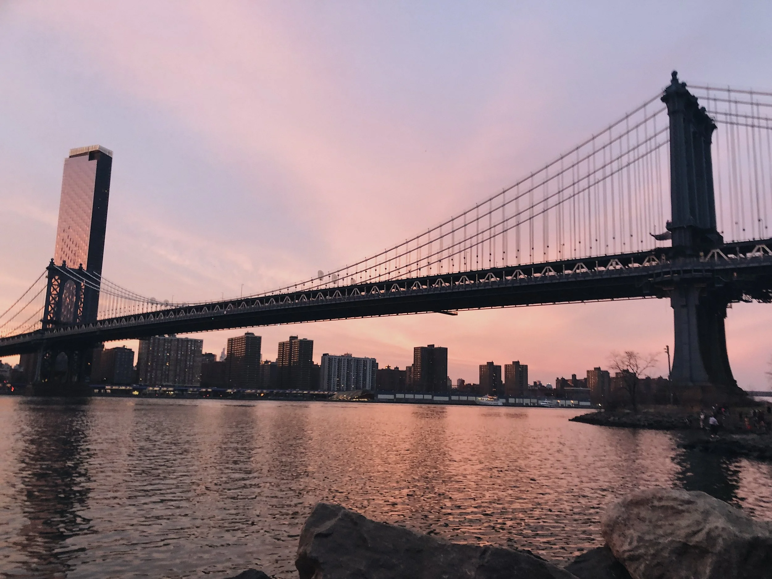 Manhattan Bridge at dusk, pink sky reflected in the East River, Brooklyn in the foreground