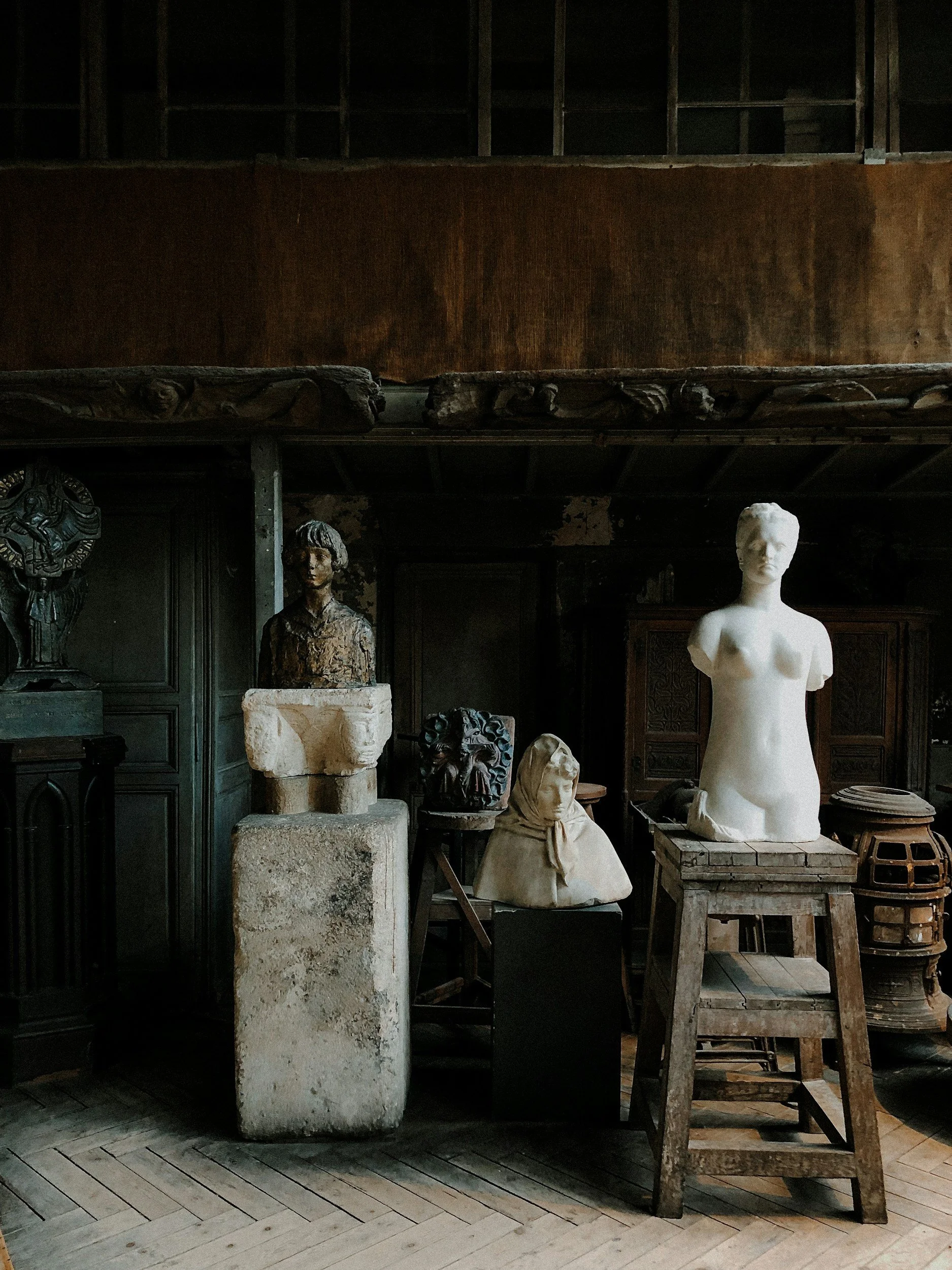 Classical sculpture fragments in a dark studio, including a white armless torso on a crate
