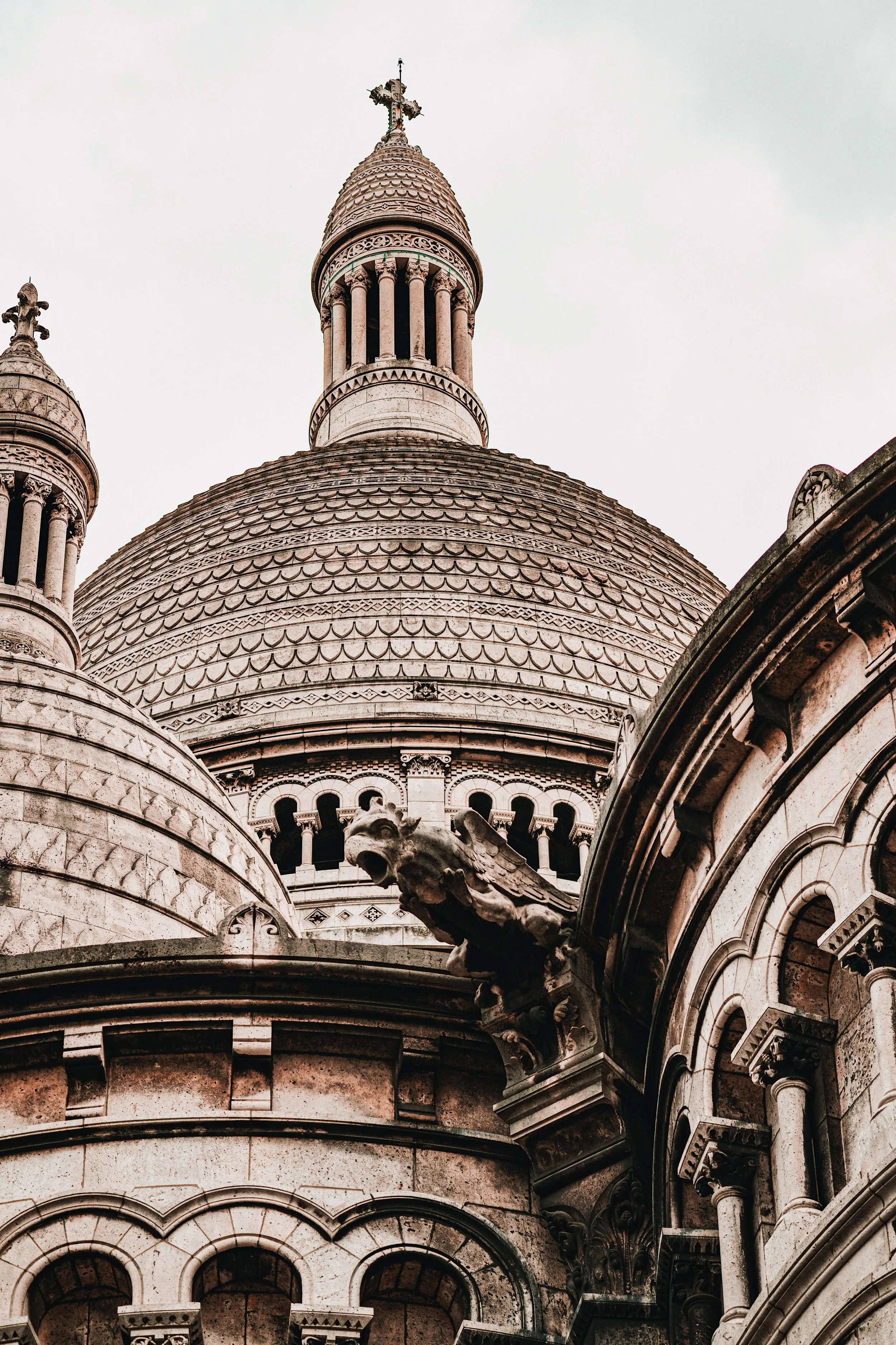 Close-up of the ornate dome of Sacré-Coeur basilica in Montmartre, stone carvings and a cross visible against an overcast sky