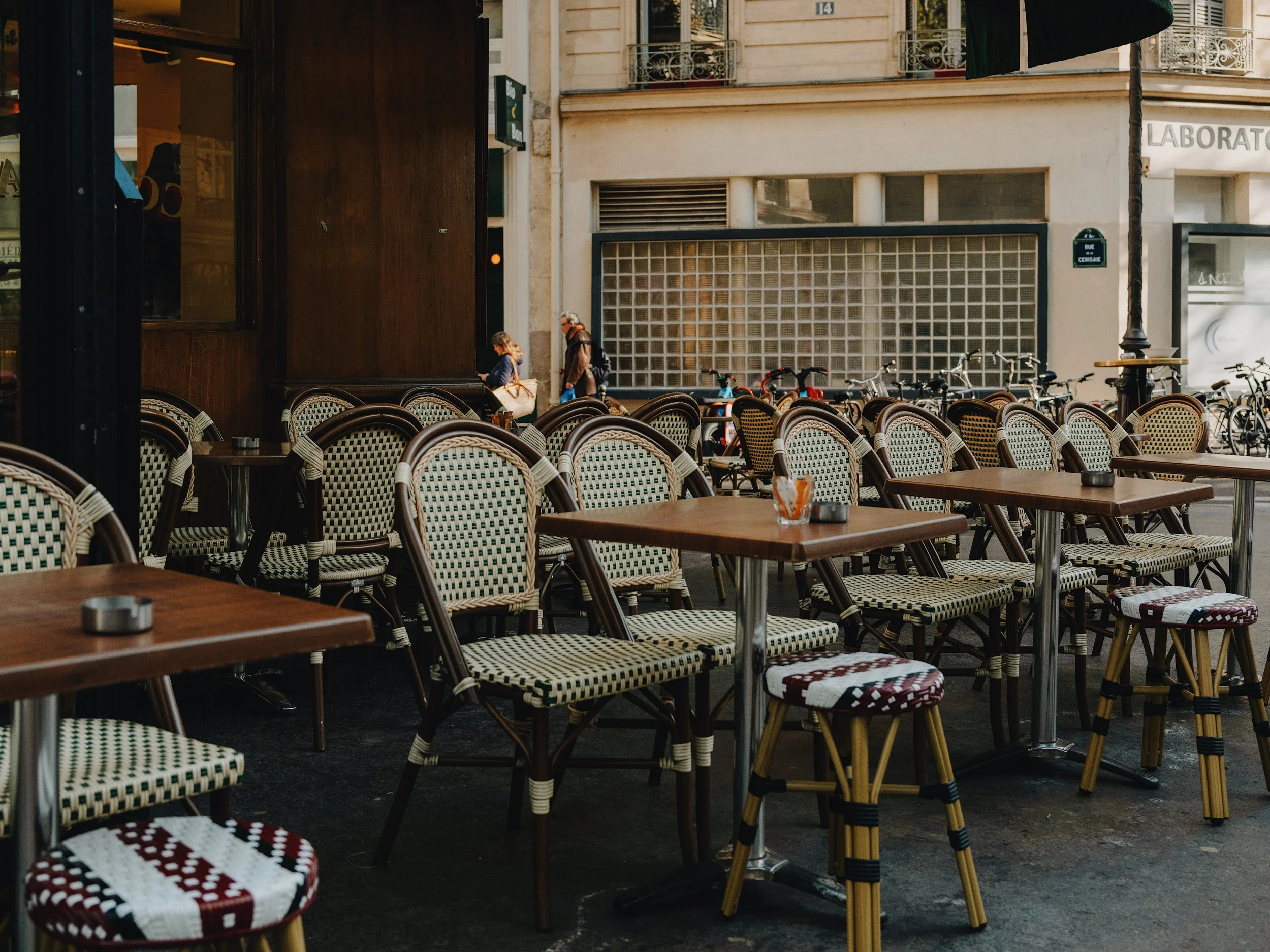 Empty café terrace with rattan bistro chairs and small tables on a Parisian pavement, shopfront visible behind