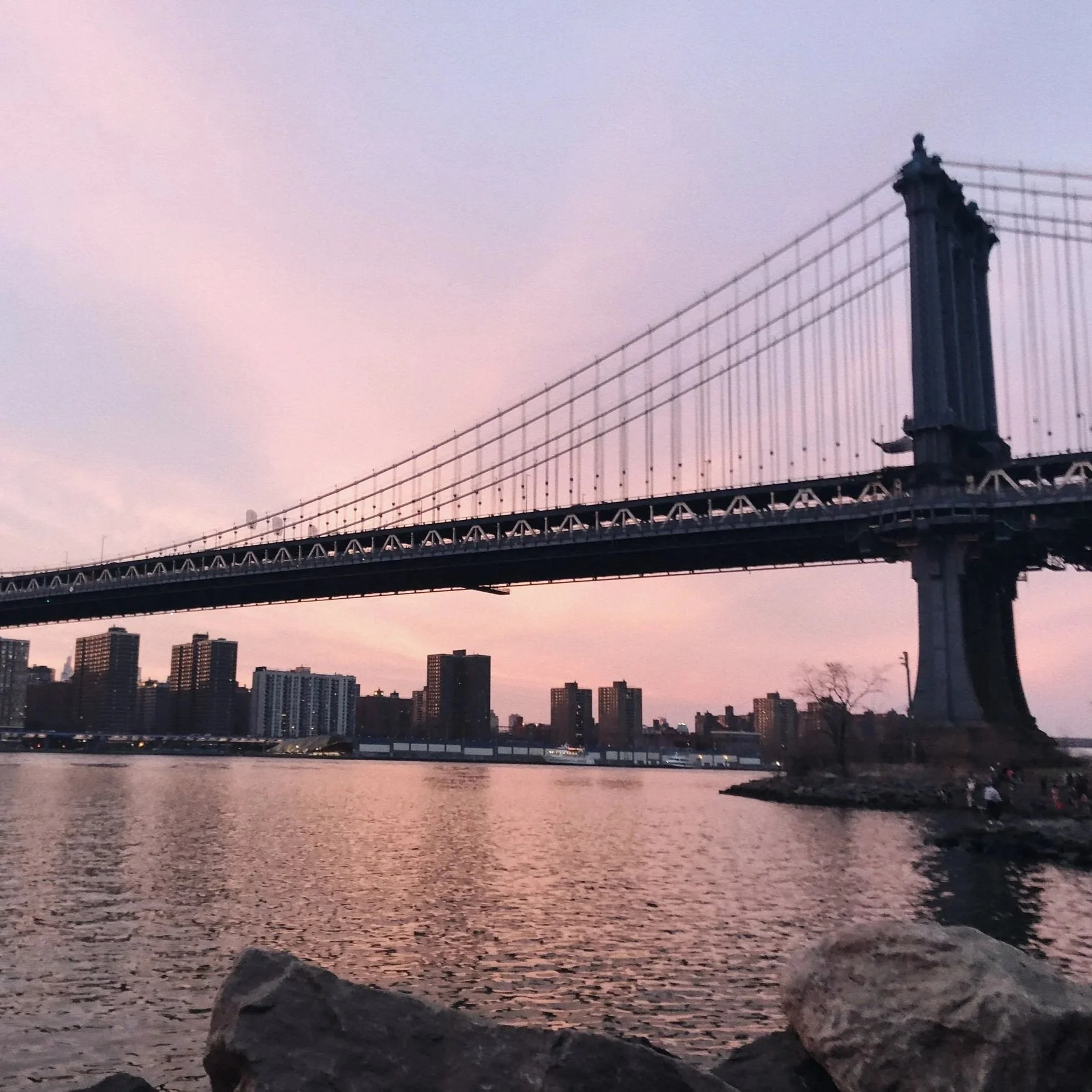 Manhattan Bridge viewed from Brooklyn waterfront at sunset, pink sky reflected in the East River