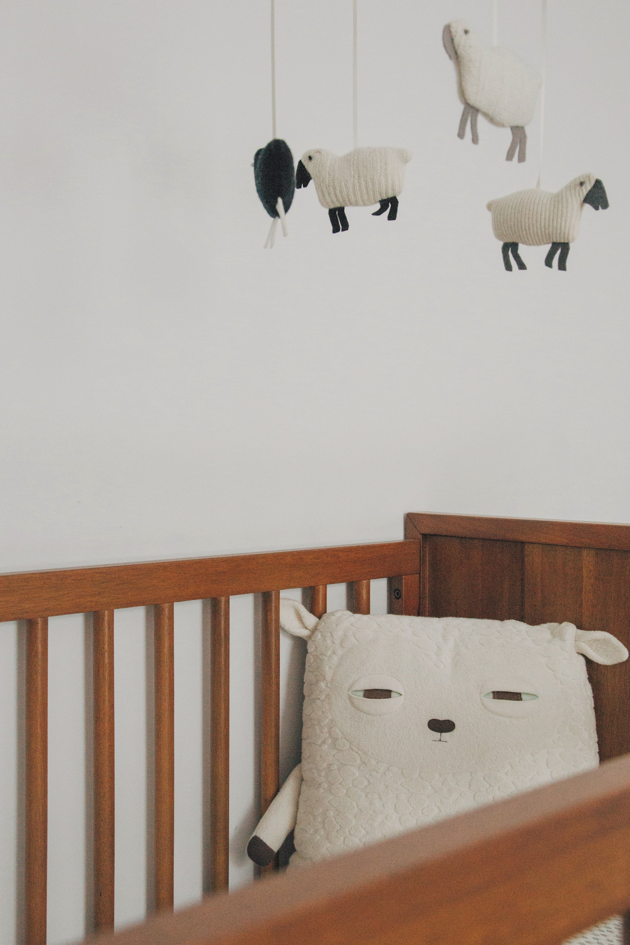 Decorative sheep and bird plush toys hanging on a white wall above a wooden bed with a sheep-shaped pillow in a child's room.
