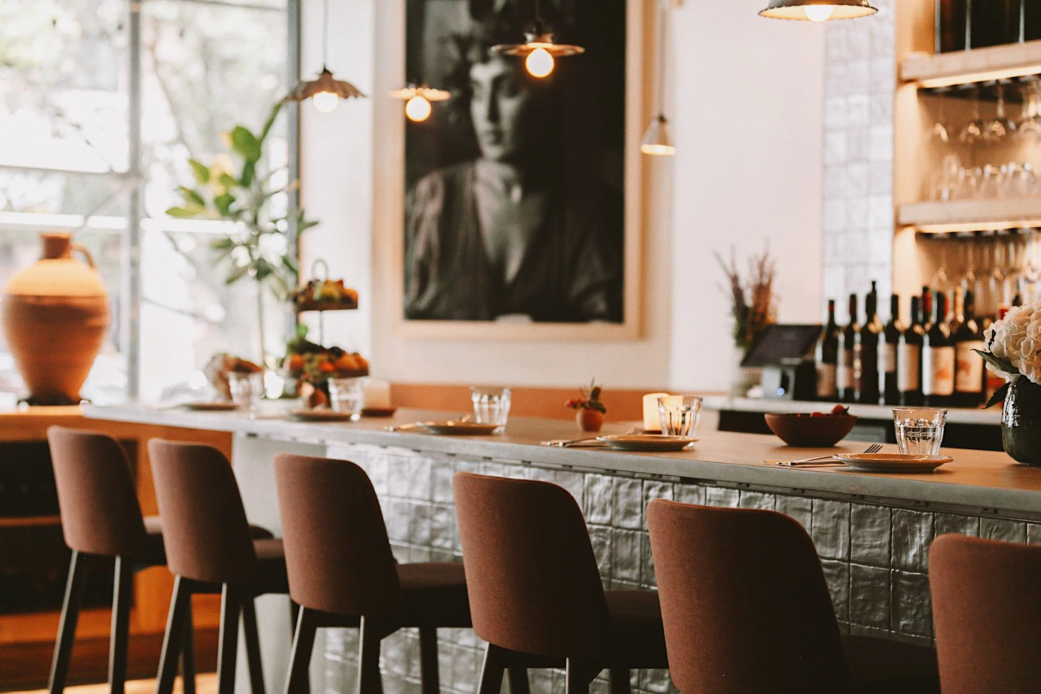 Interior of Chama Mama, Brooklyn Heights, with warm pendant lighting, a long communal table, and a large portrait on the wall