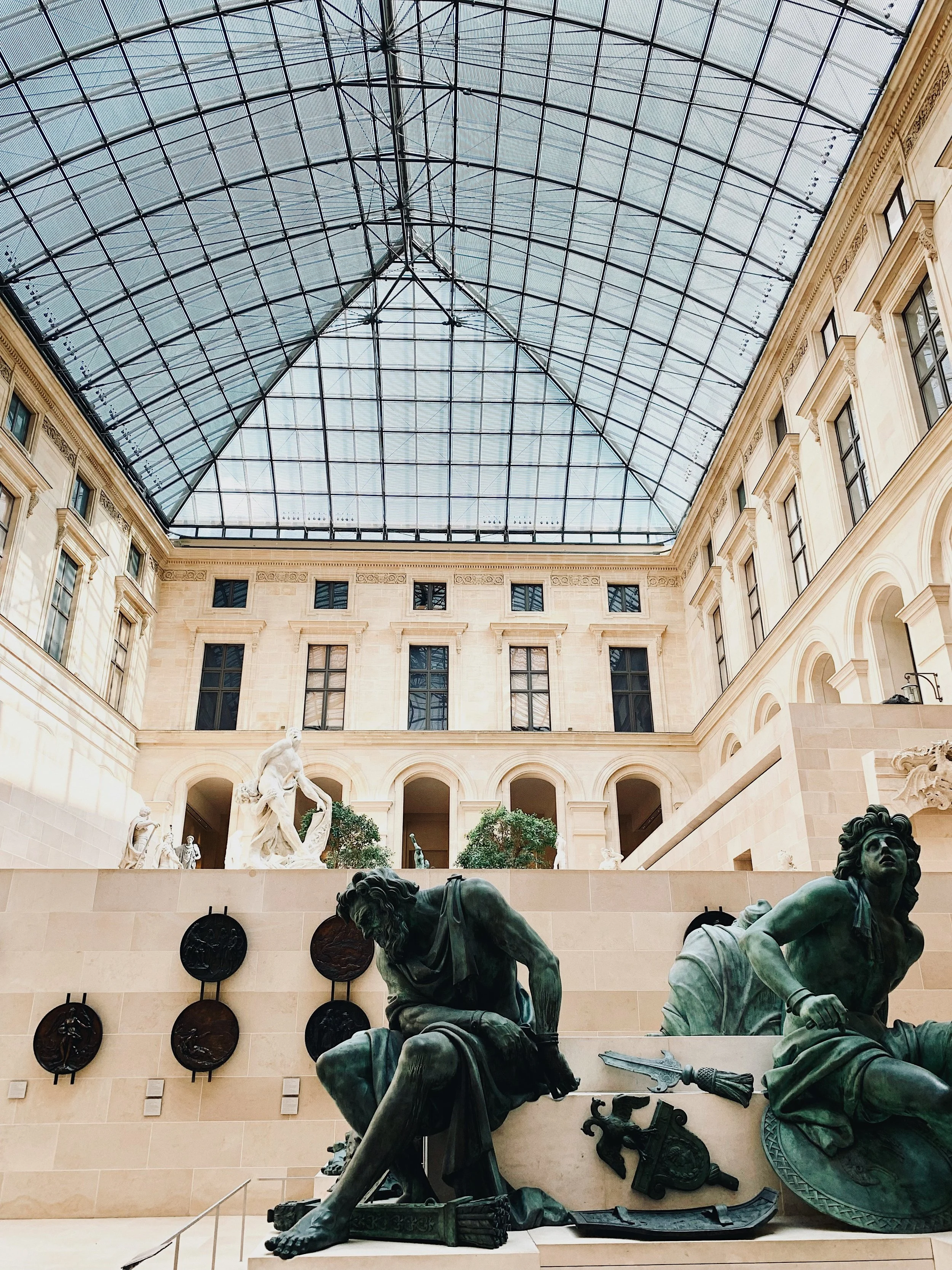 Bronze sculptures in the foreground of the Louvre's Cour Marly, with the glass roof and stone arcade of the museum visible behind
