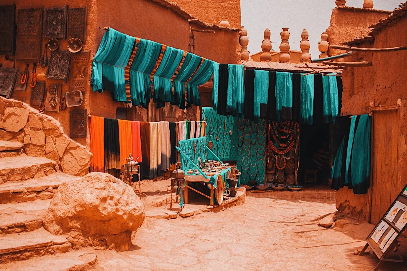 Teal and orange textiles hanging outside a terracotta-walled shop in the medina