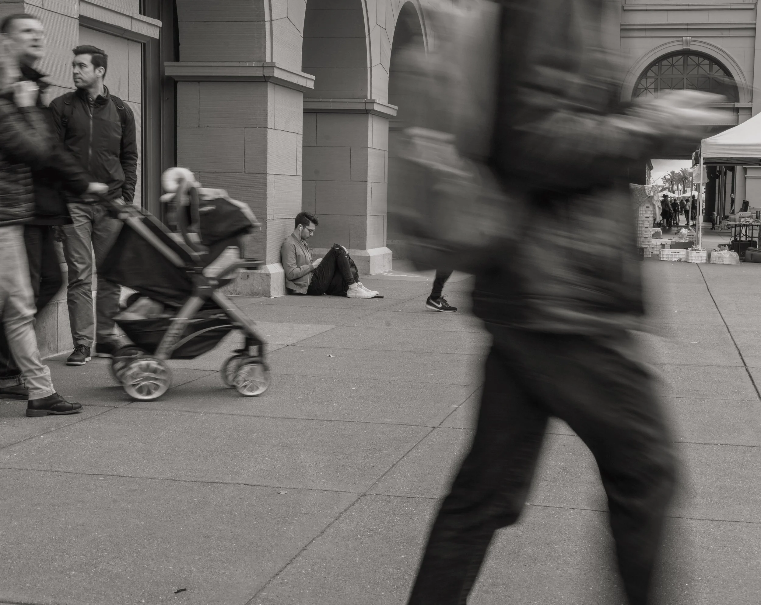 A parent pushing a stroller down a city street, captured in black and white.