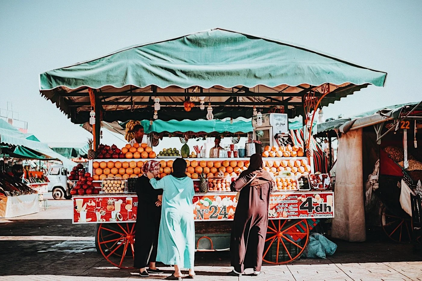 Two women ordering fresh juice from a red-wheeled cart in Jemaa el-Fna