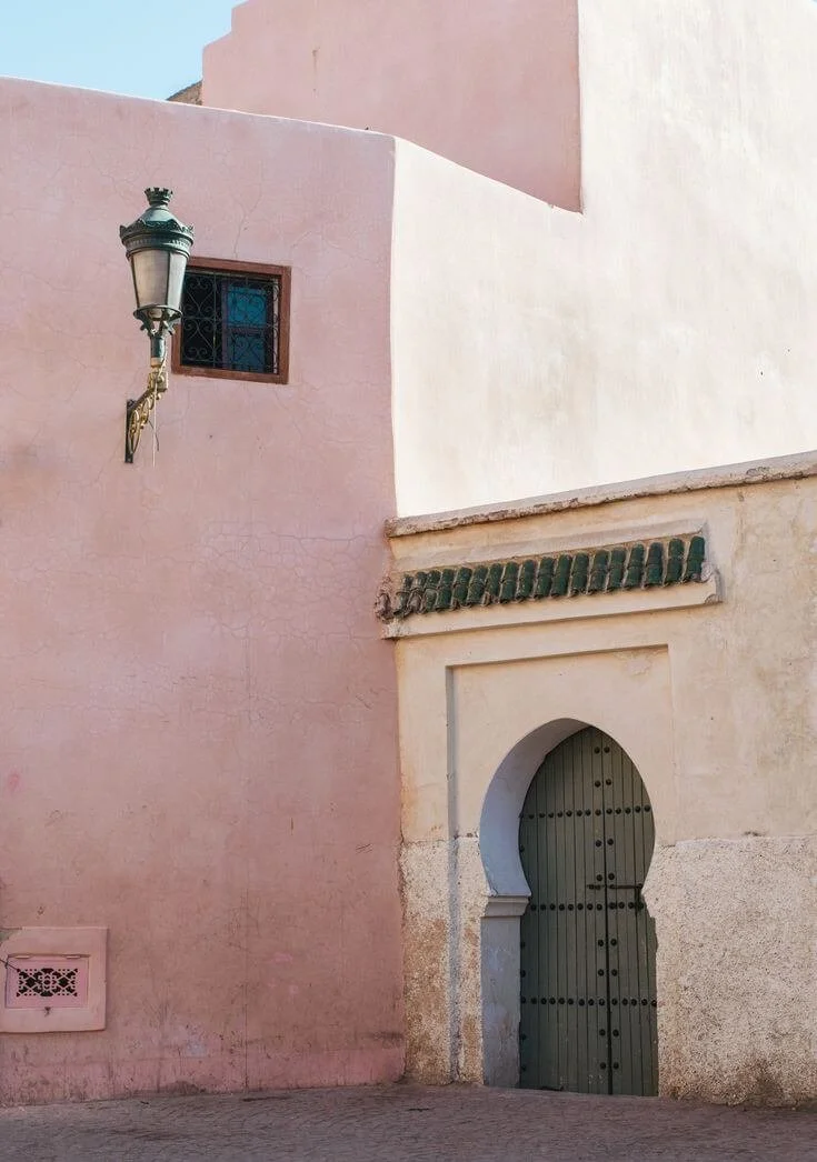 A sunlit arched green door set into pale plaster walls.