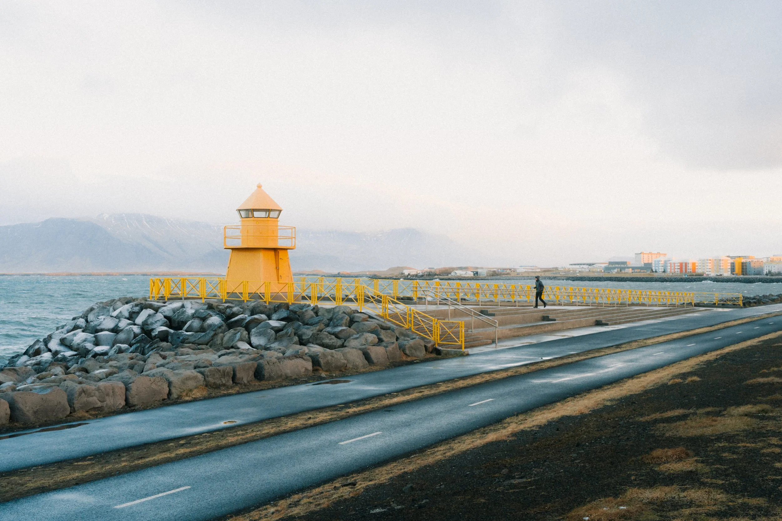 Man walking in winter to yellow light house in Reykjavik bay in Iceland