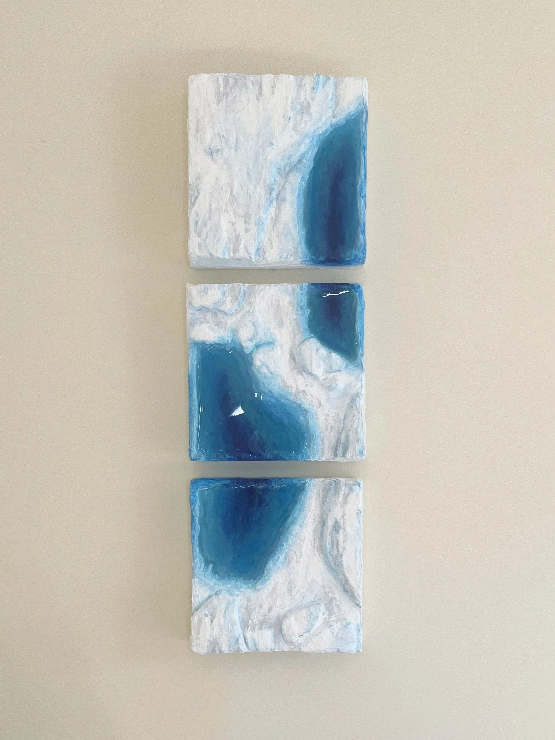 Three square tiles depicting blue ponding, stacked vertically on a beige surface.