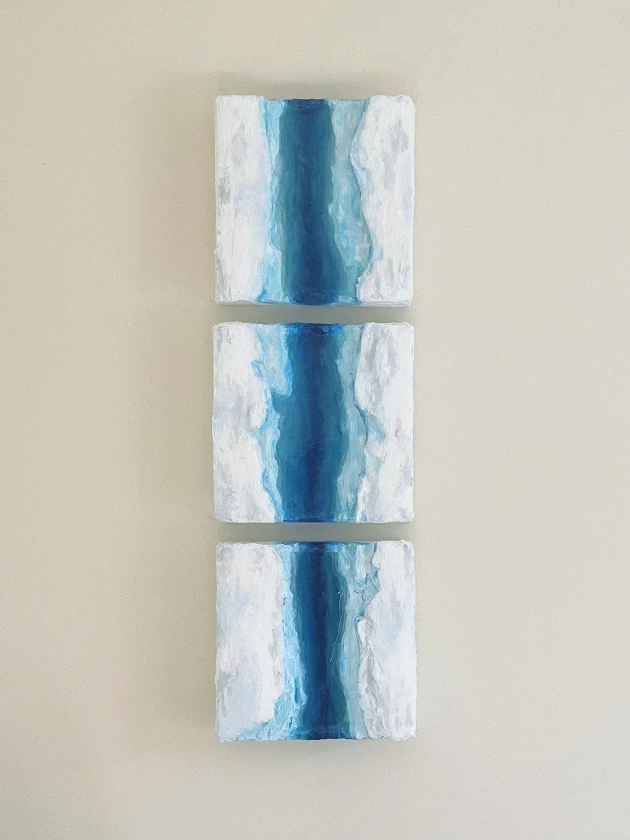 Painting of blue river depth on white textured backgrounds, arranged vertically on a white wall.