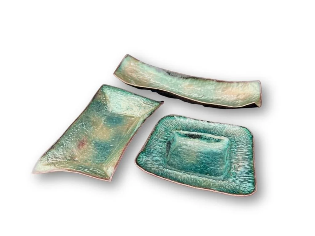 Set of three ceramic dishes with an iridescent glaze, one rectangular and two square-shaped, on a white background.