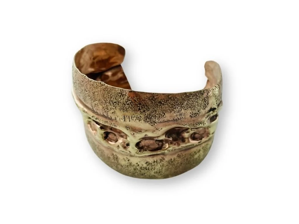 Close-up of a wide, metallic brass cuff bracelet with a textured, aged finish on a white background.