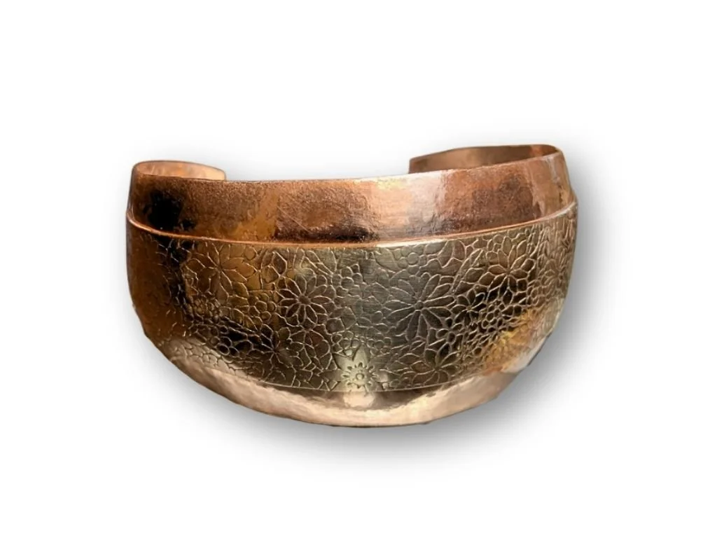 A metallic cuff bracelet with intricate floral engravings.