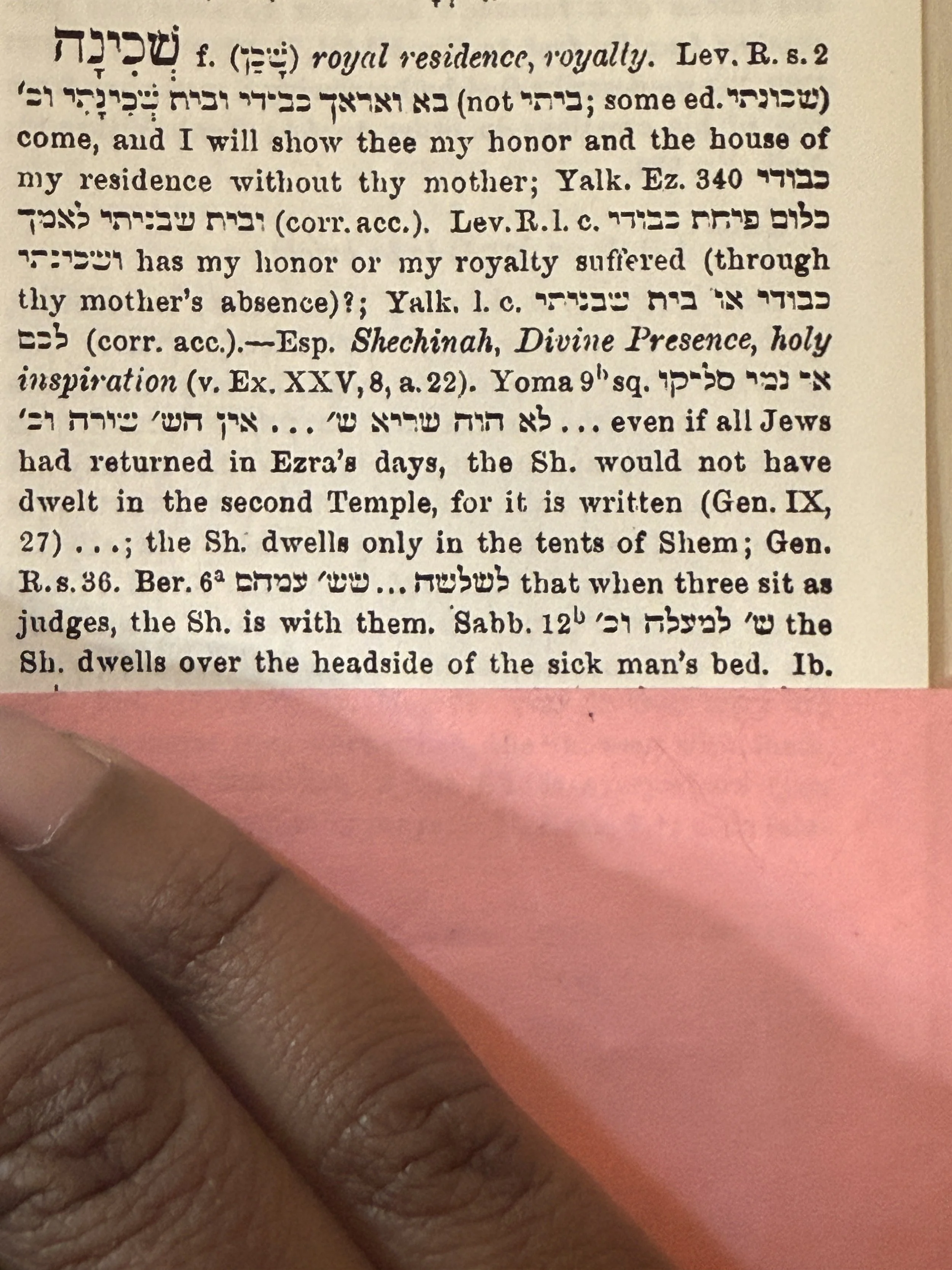 Close-up of a text page with Hebrew and English writings, partially covered by a pink paper and a person's finger.