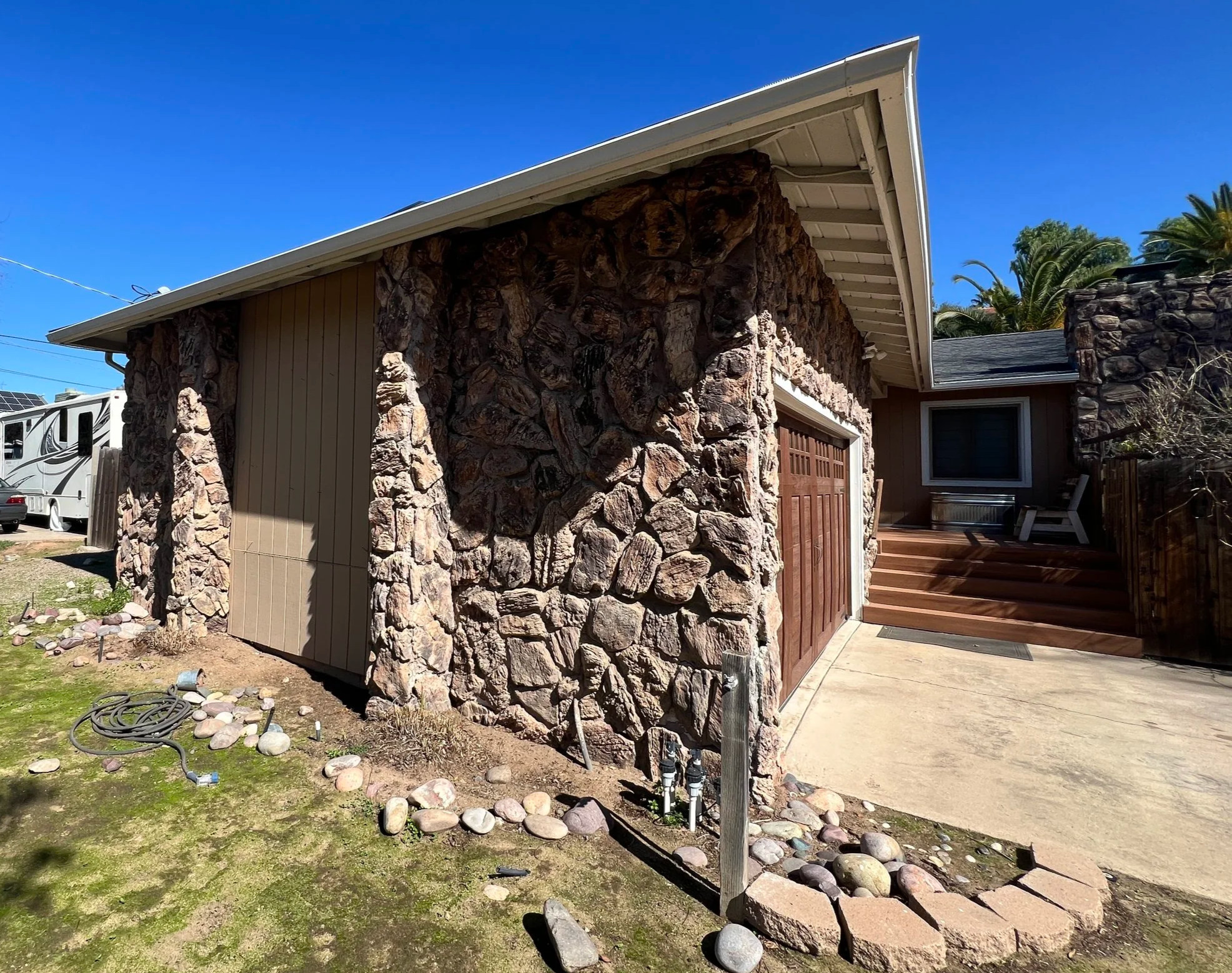 Front of house with stone and wood exterior, garage door, and wooden stairs leading to a patio with outdoor seating.