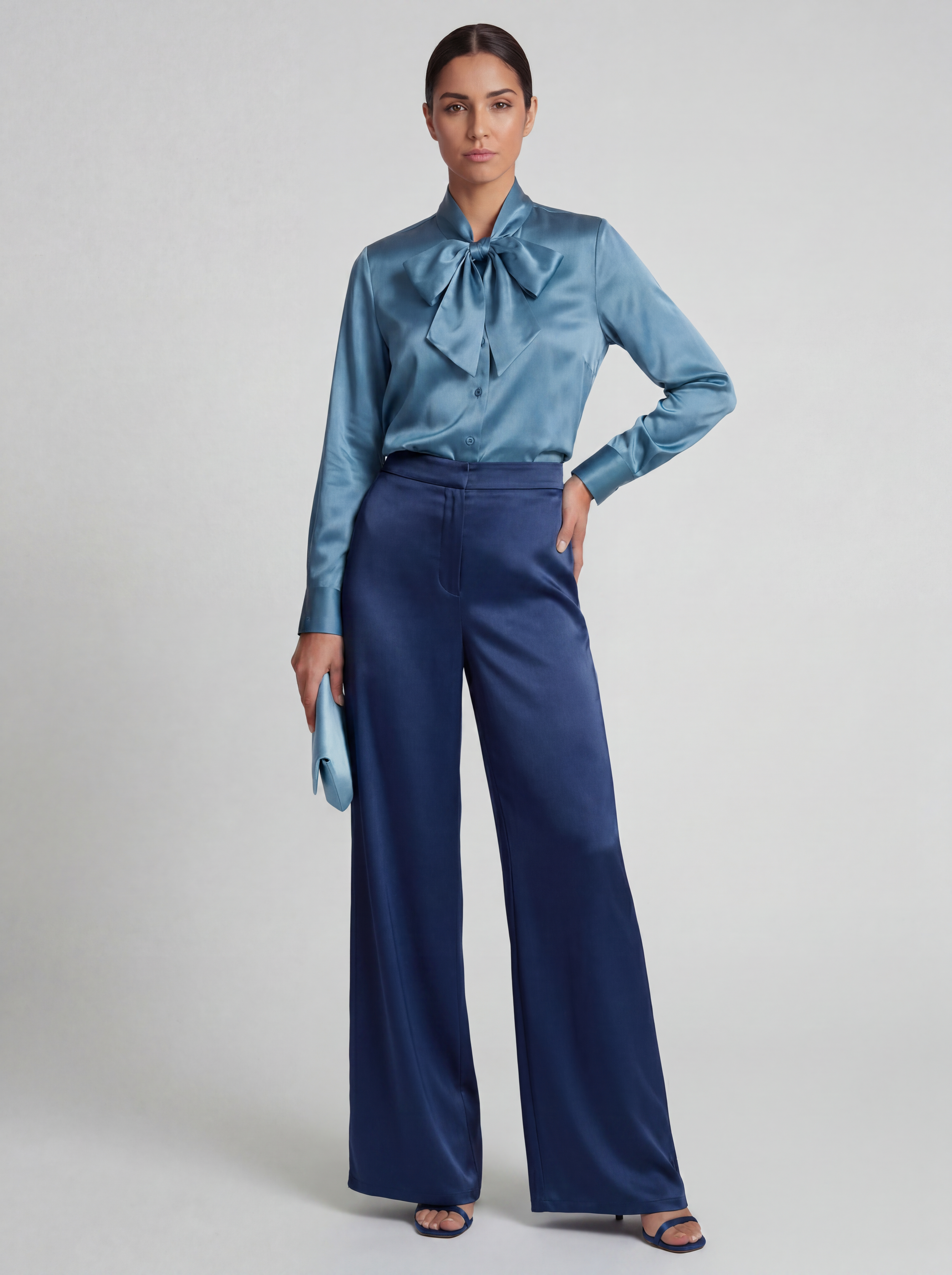 Front shot of model standing in a studio wearing a bow tie front silk shirt in Azure blue and navy blue silk wide leg pants
