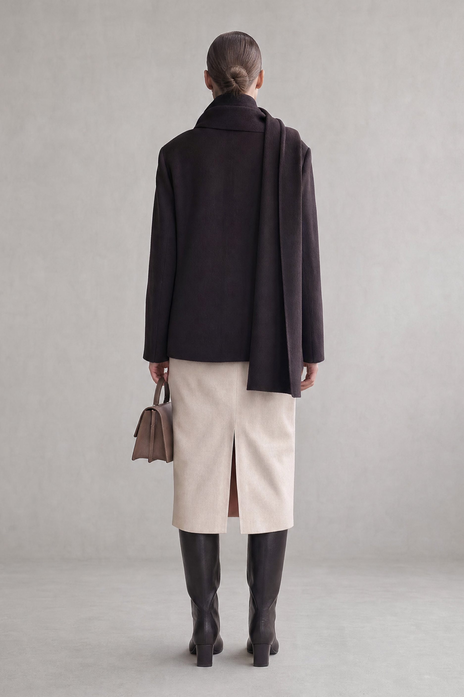 Model facing away from the camera wearing the Julia Coat over a cream sheath dress