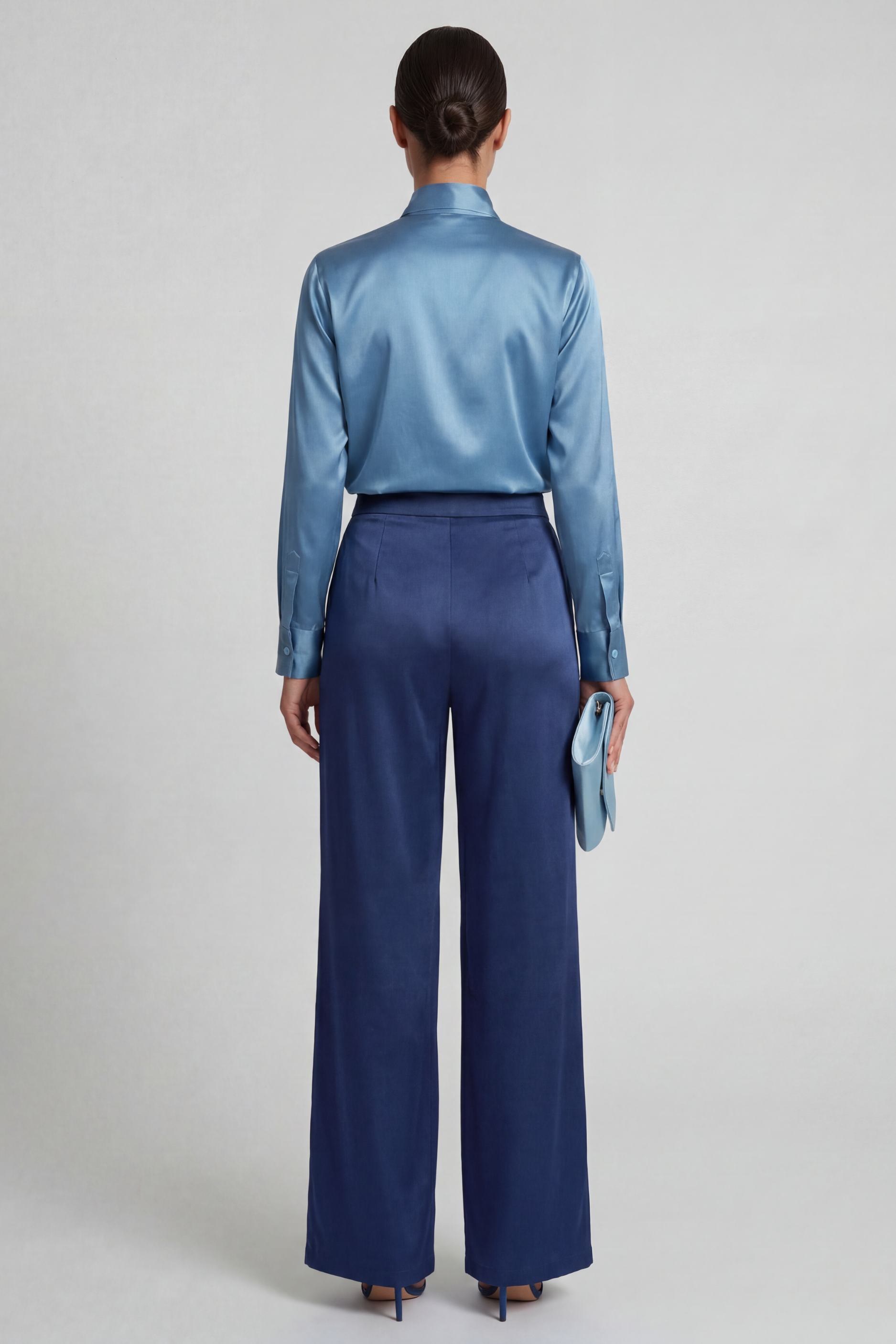 Back shot of a model standing in a studio wearing the bowtie front shirt with blue silk wide leg pants