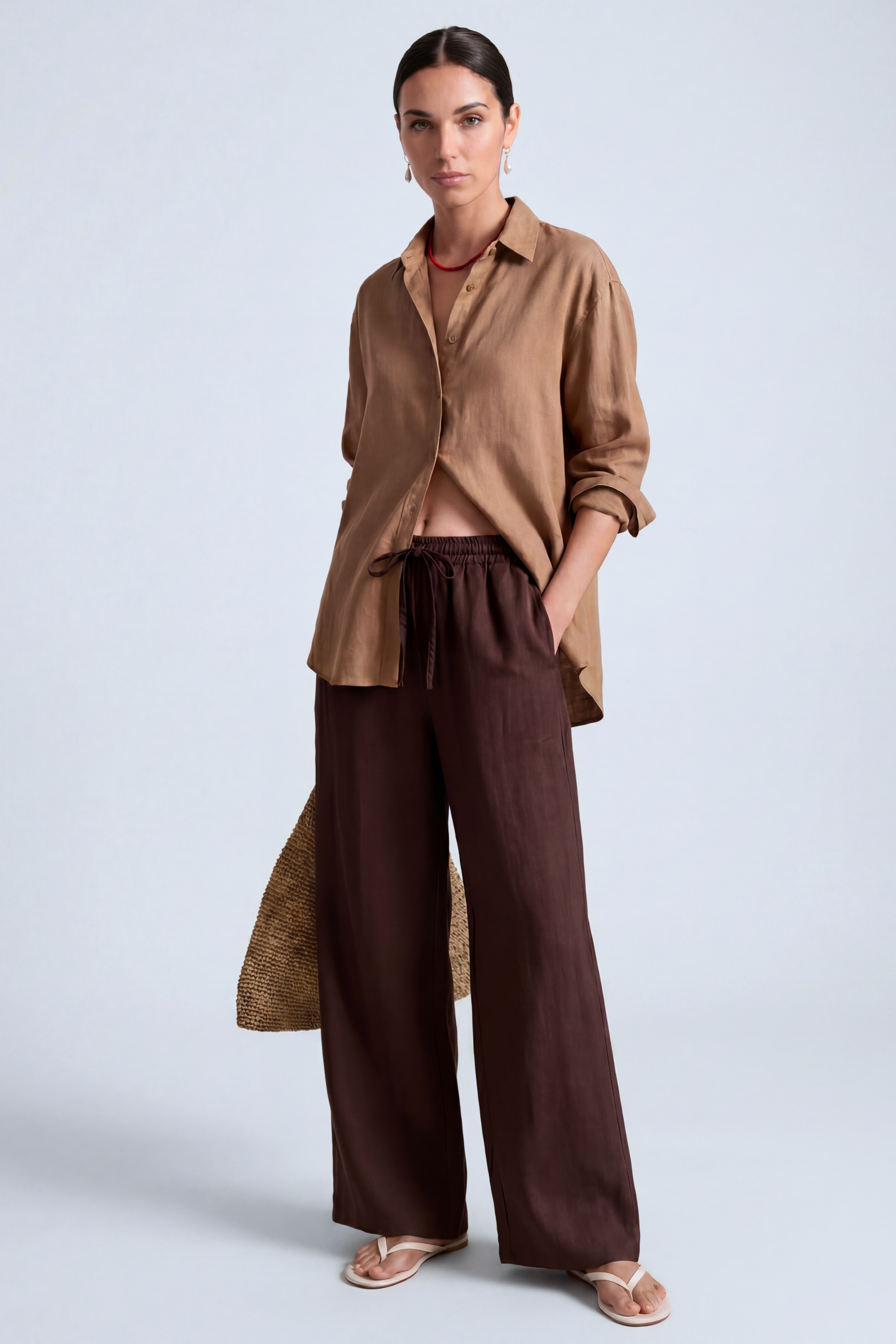 Brunette model in a studio wearing a loose linen shirt in camel color with chocolate brown drawstring linen pants
