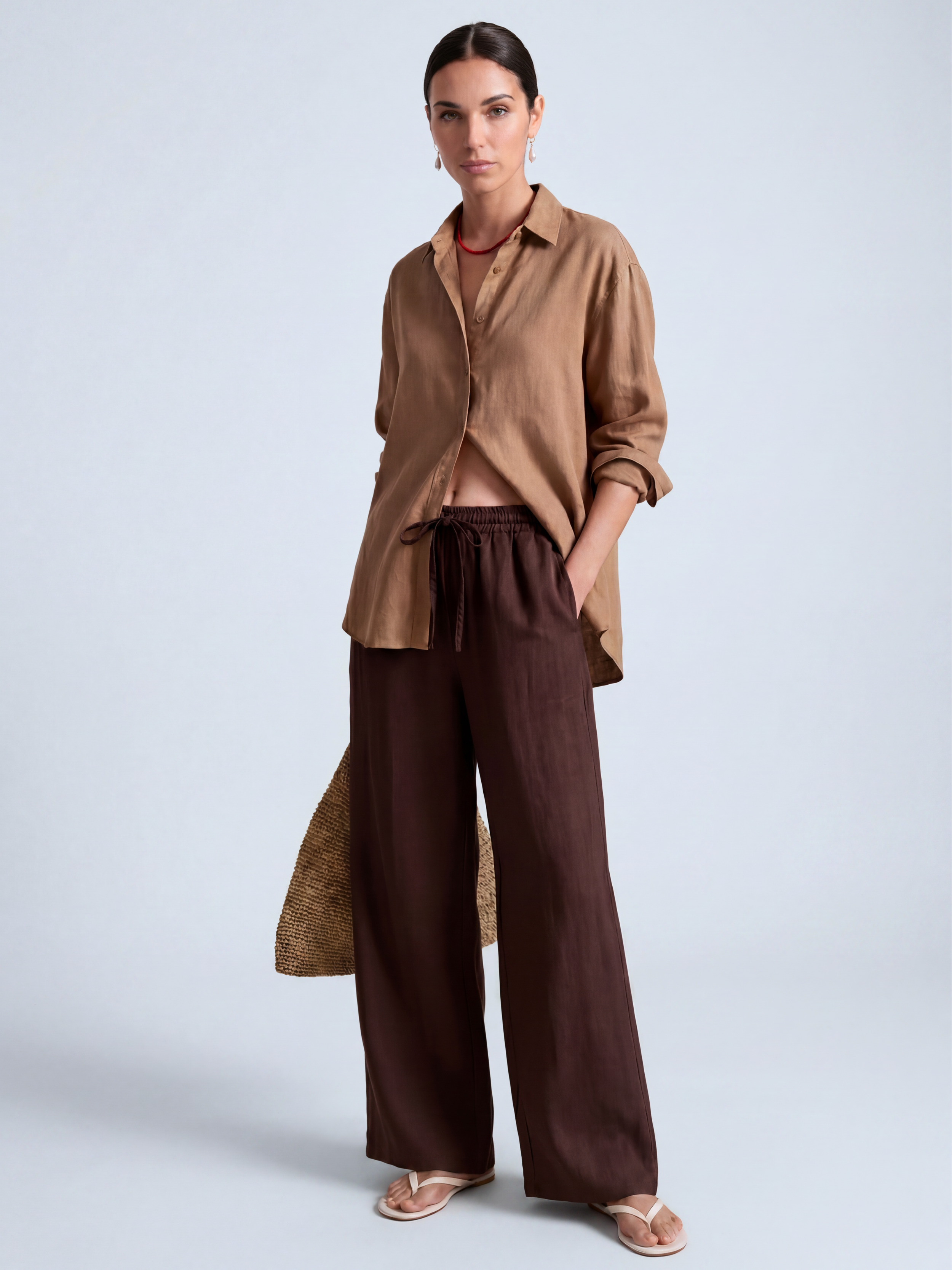 Brunette model in a studio setting wearing wide leg brown linen pants and a camel colored linen shirt