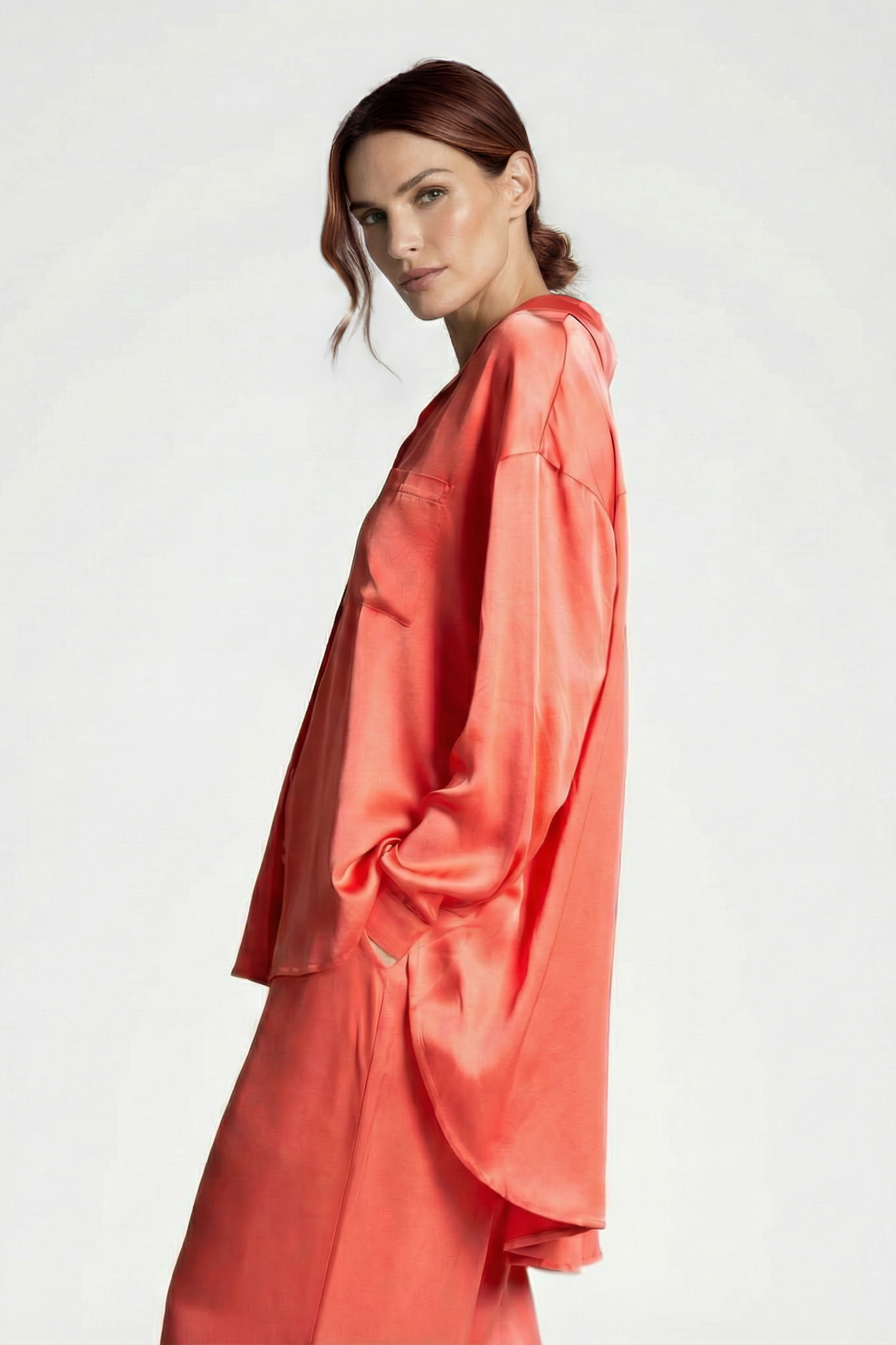 Brunette model standing in a side pose in a photography studio wearing a silk coral oversized lounge set