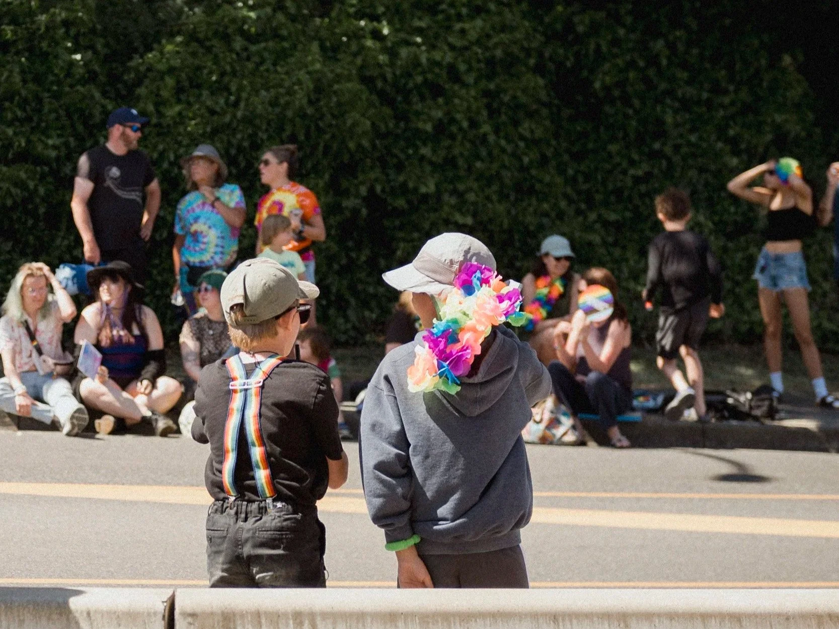 to young children wearing rainbows watching a pride parade.