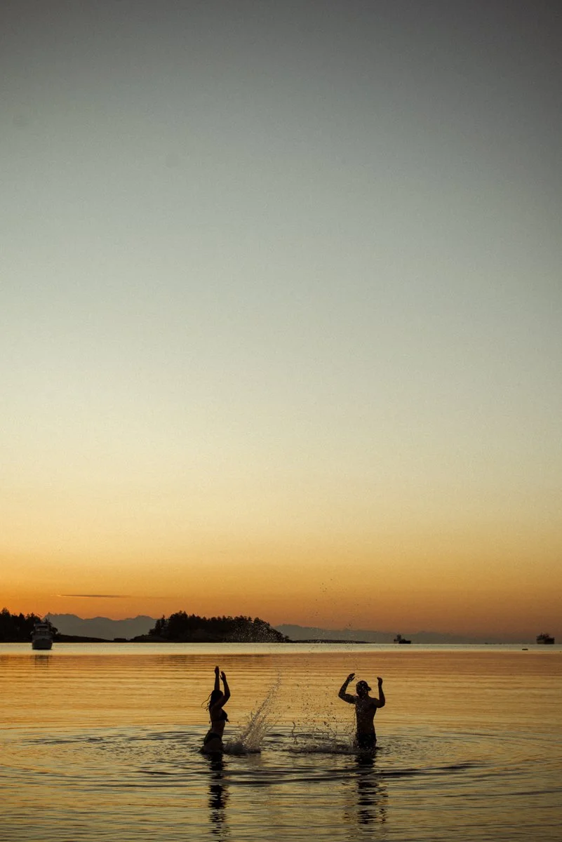 two people splashing in the water just before sunrise.