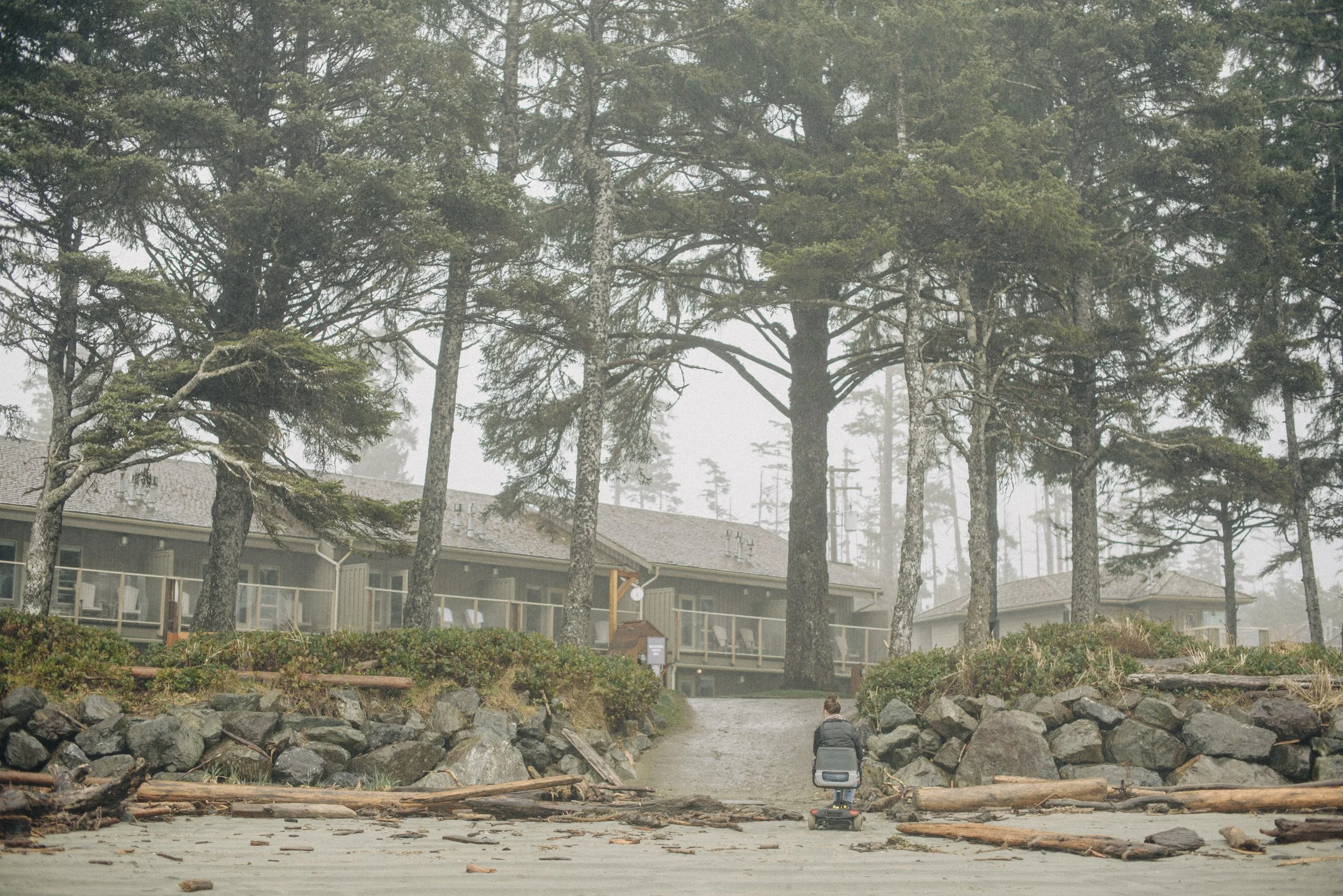 A woman coming up from the beach in her electric scooter on a misty day in Tofino, British Columbia.