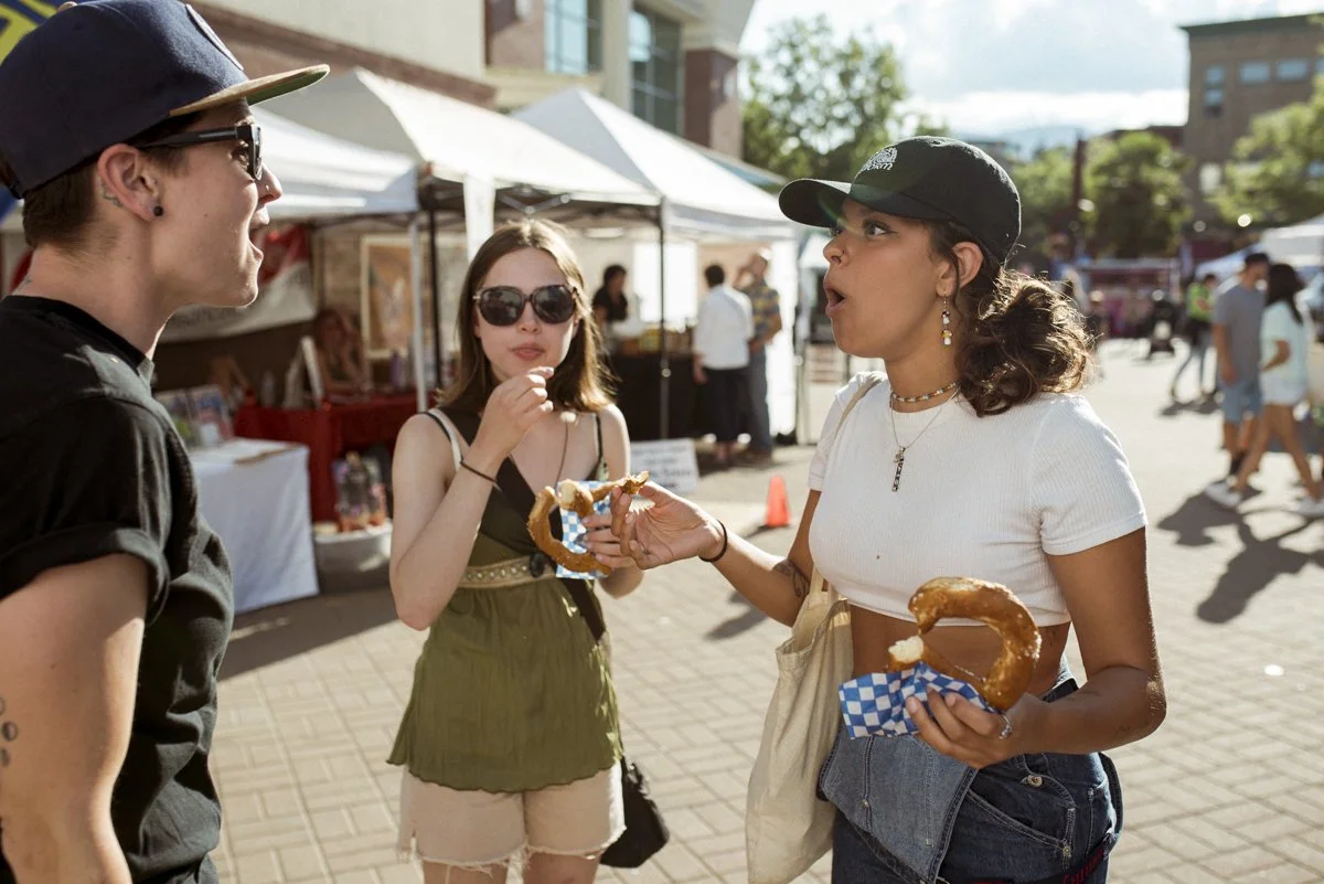 3 friends creating each other at an outdoor event. two of the friends are wearing hats and the other is wearing dark glasses.