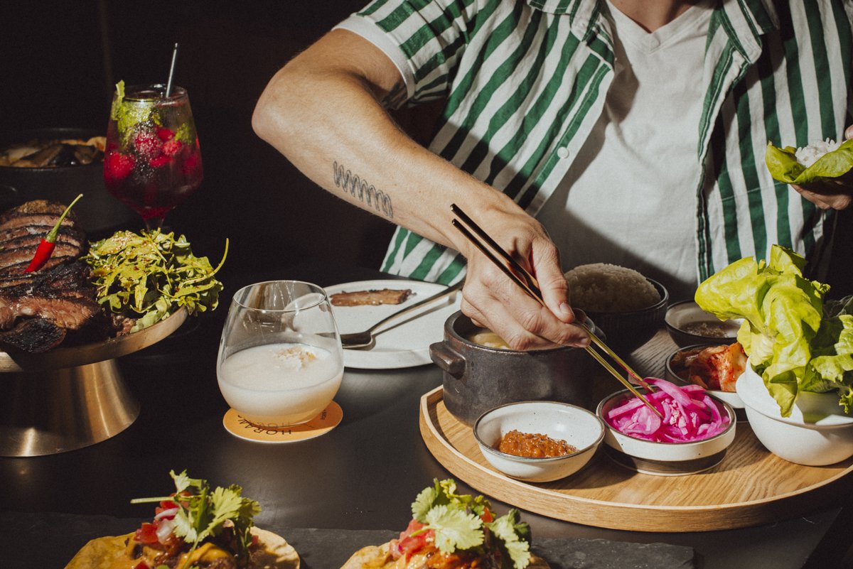 a person reaching for the pickled onions to add to their lettuce wraps. the full frame of the image shows food and drinks.
