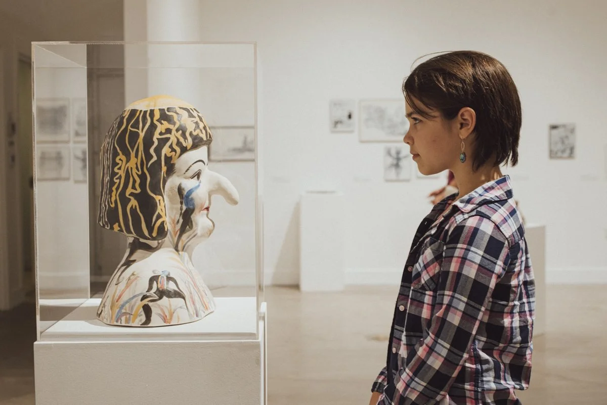a young person standing in front of a sculpture of a person. They are looking directly into each other's eyes.