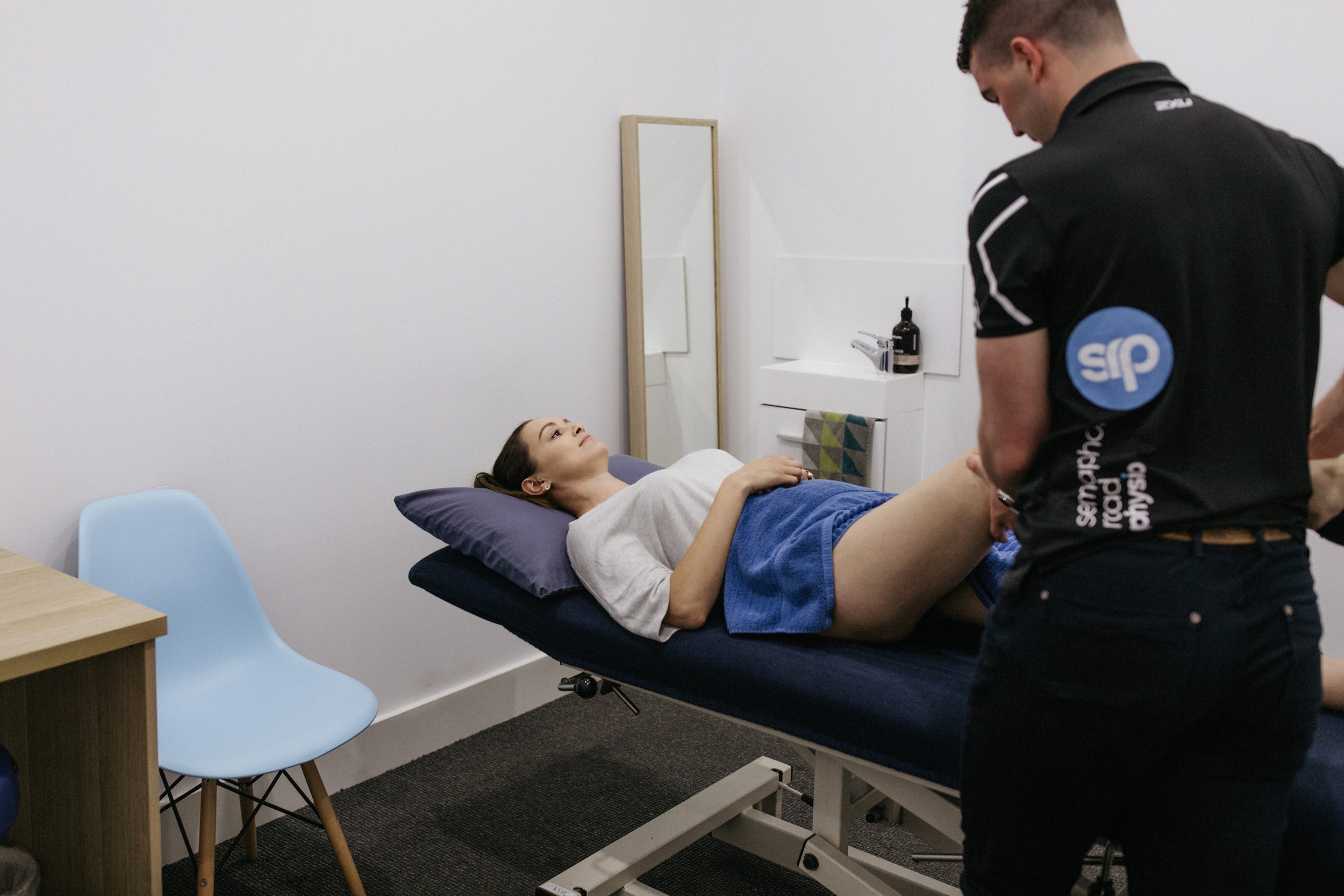 A woman lying on a medical examination table with her legs elevated, being examined by a healthcare worker in a clinical room.