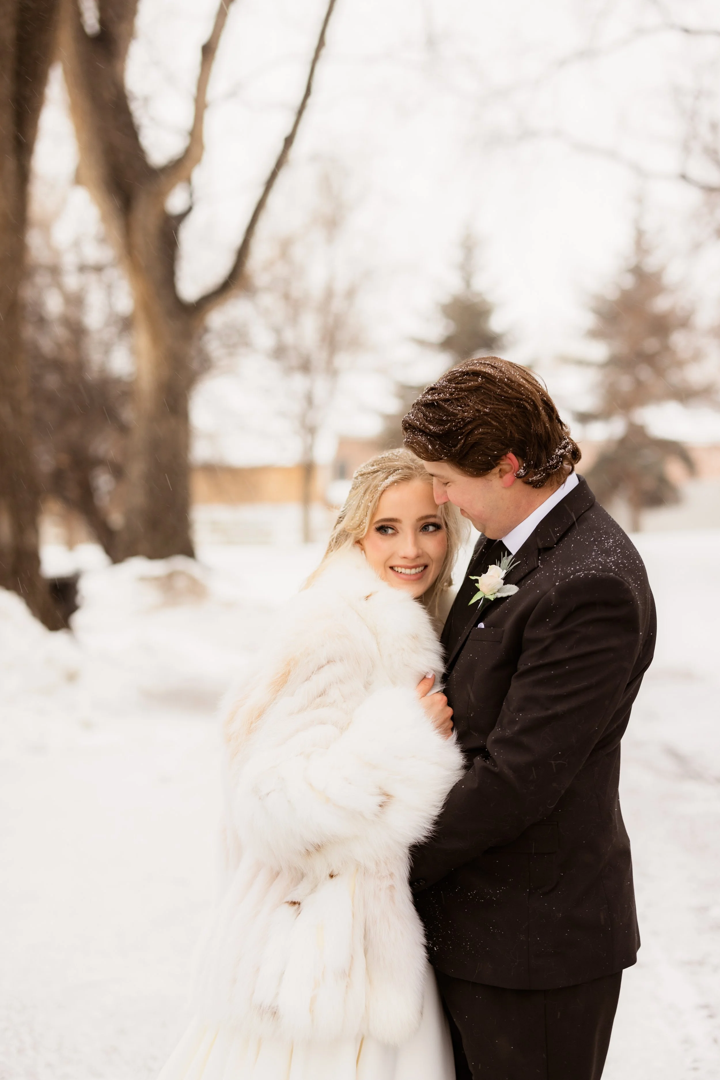 Bride and groom in winter, embracing outdoors in a snowy landscape.