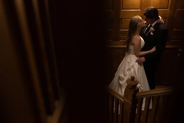 A bride and groom sharing a kiss on a staircase in a dimly lit room.