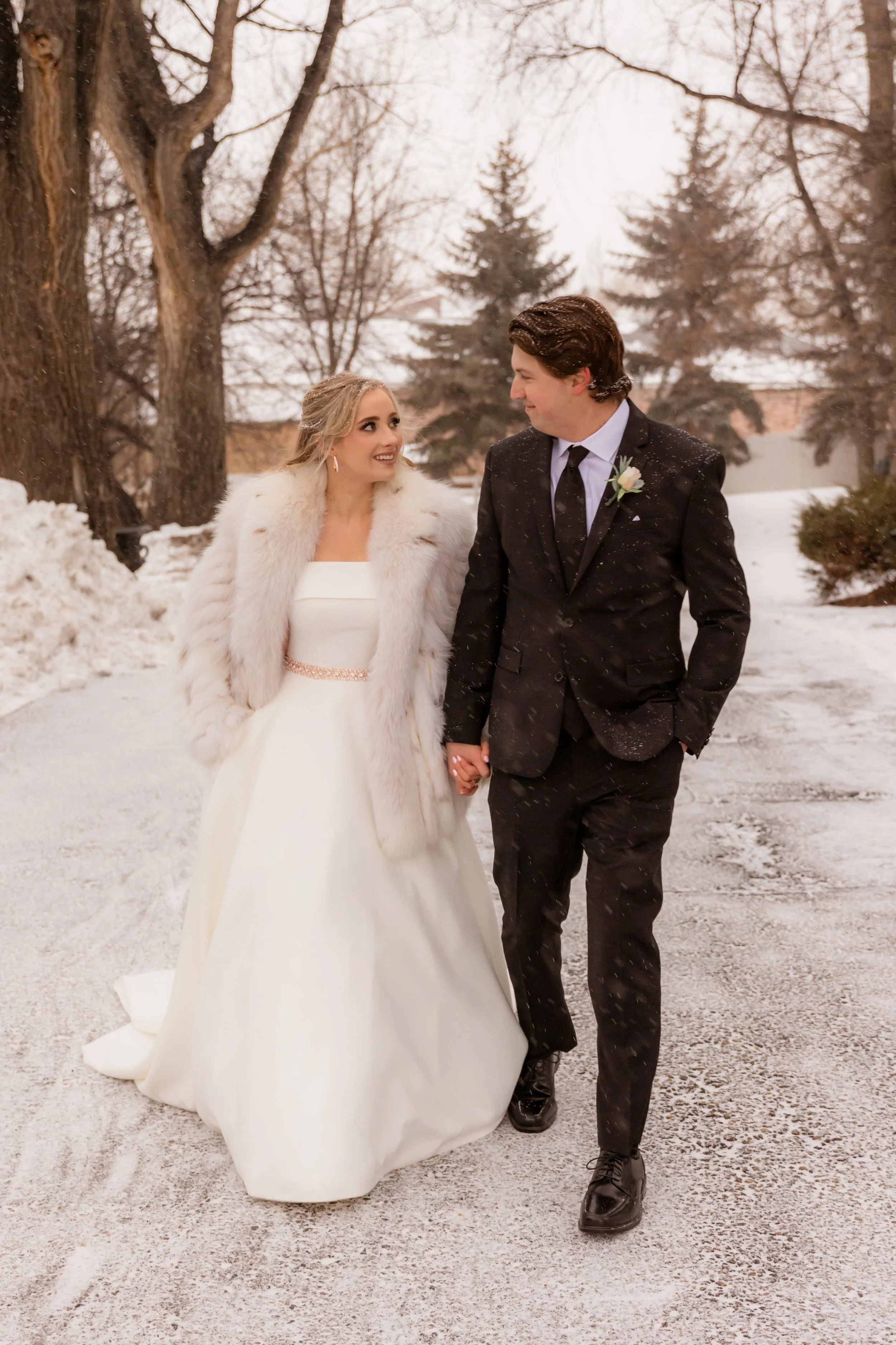 A bride and groom holding hands and walking outdoors in a snowy winter landscape.