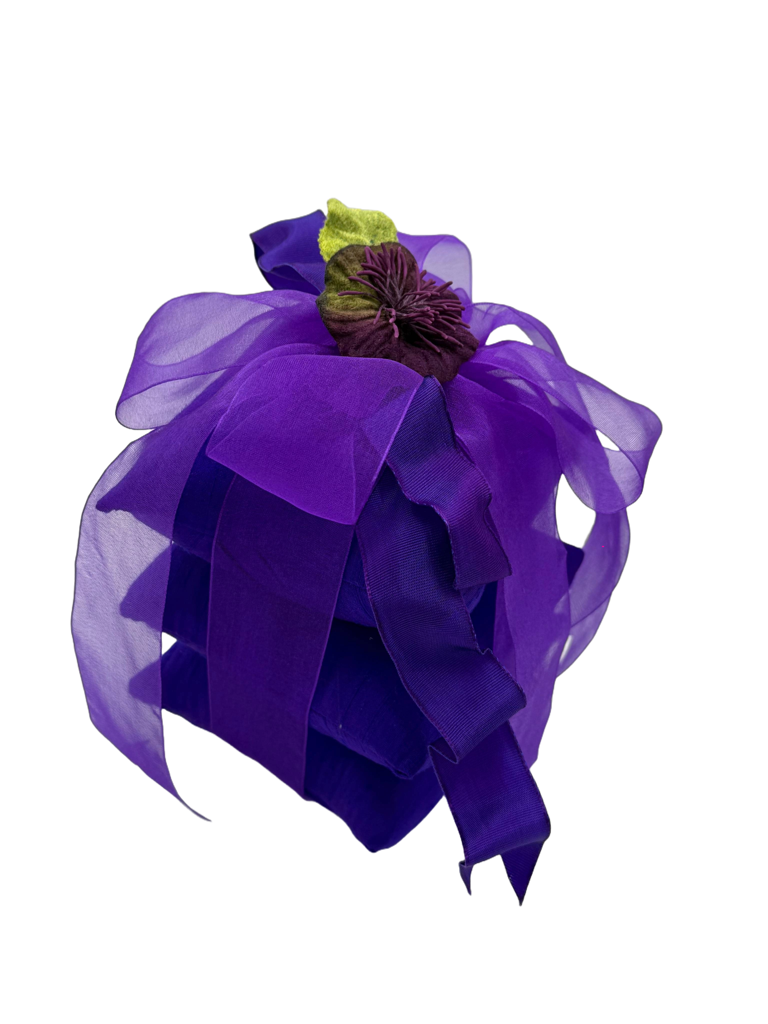A purple wrapped gift with a fabric flower and leaf decoration on top.