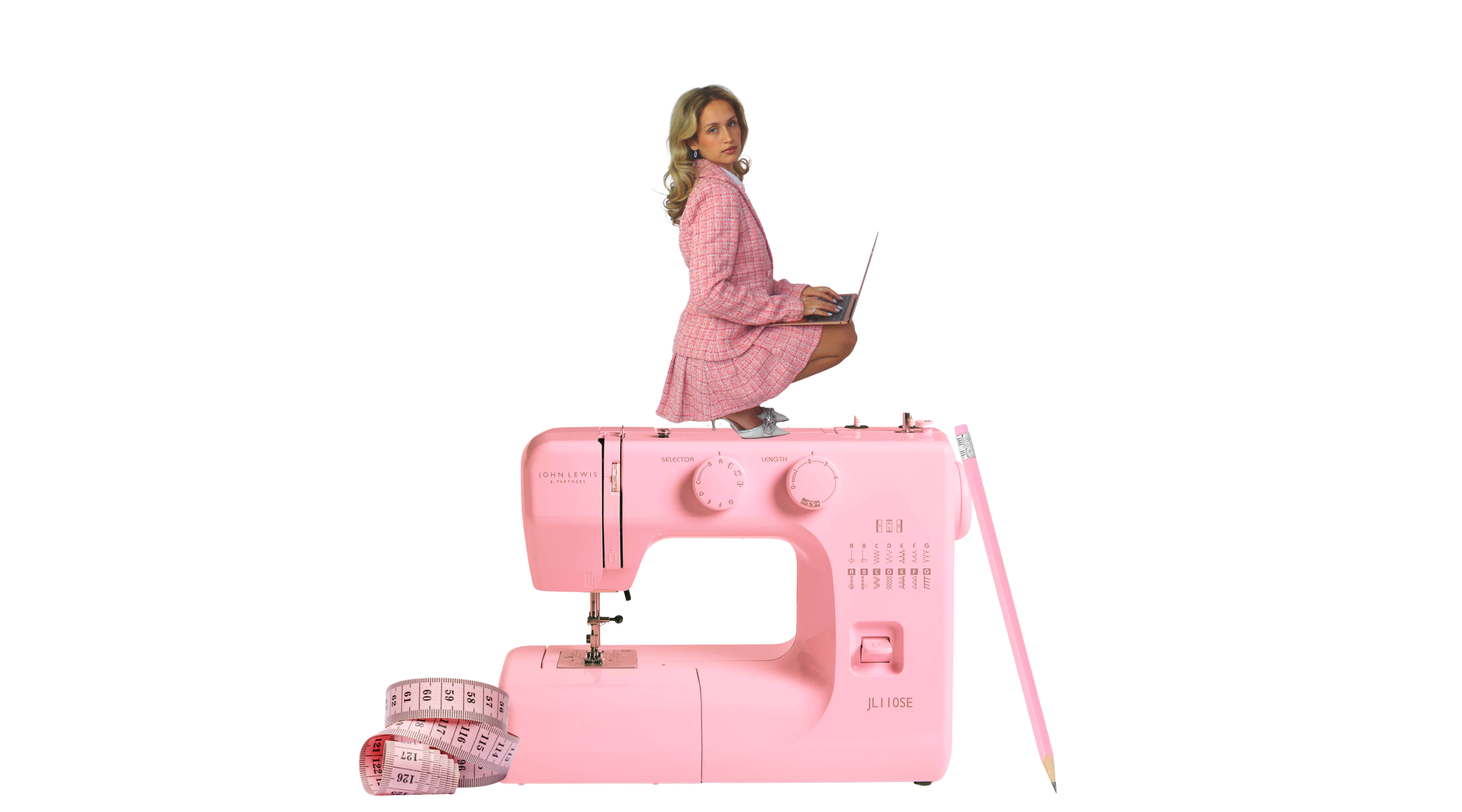 A woman in a pink plaid suit squatting on a pink sewing machine while working on a laptop.