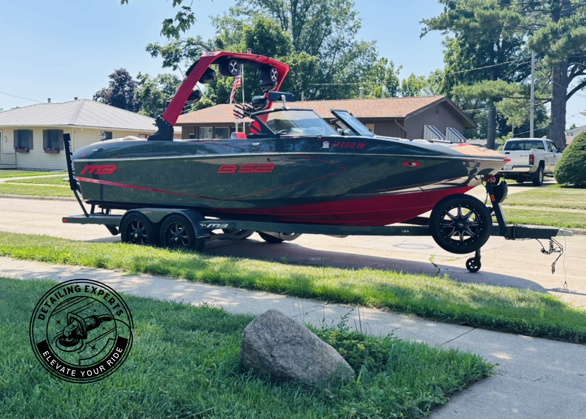 A black and red speedboat on a trailer parked on a residential street with houses and trees in the background.