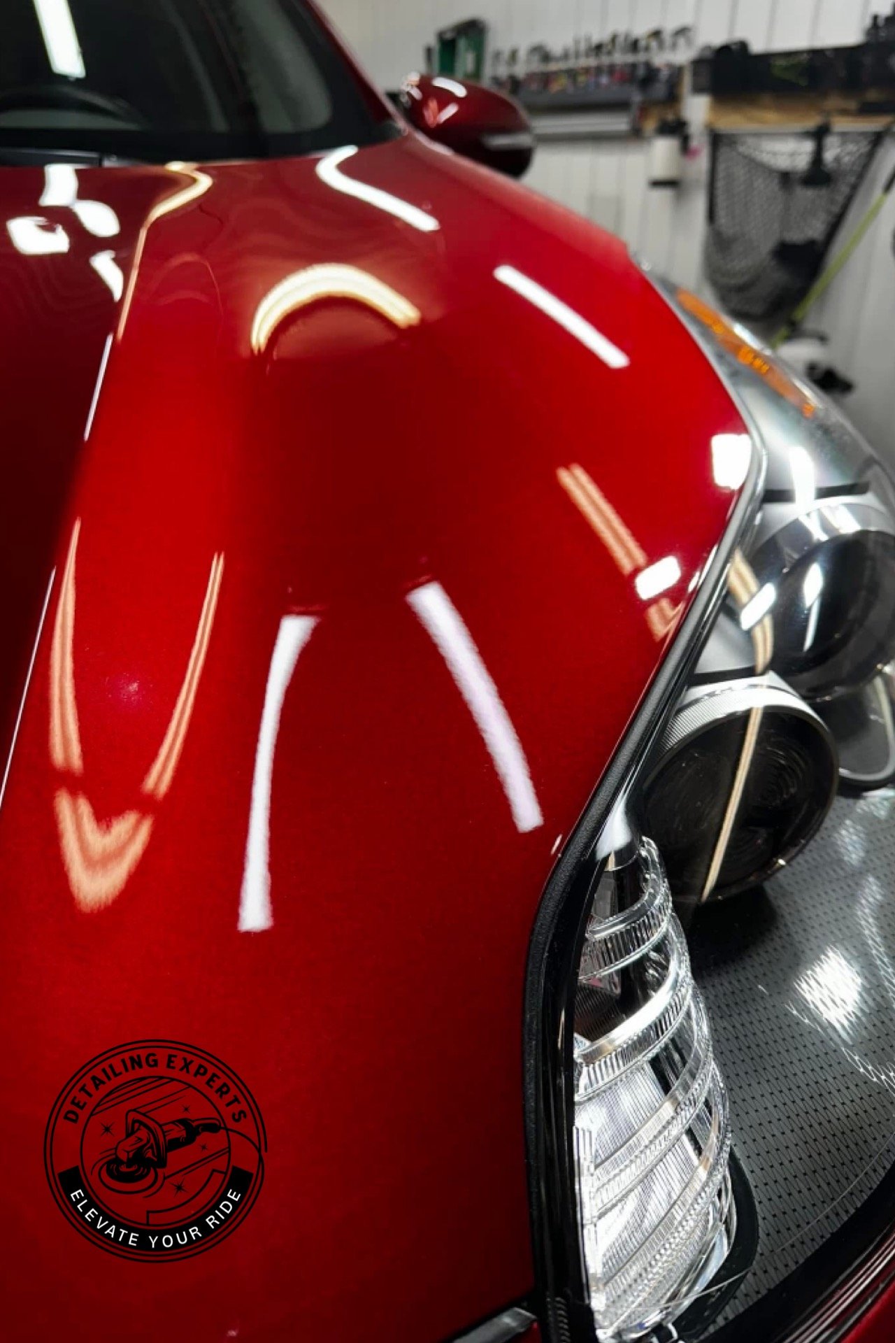 Close-up of a shiny red car in a garage, showing part of the front with clear headlights and reflections on the surface.