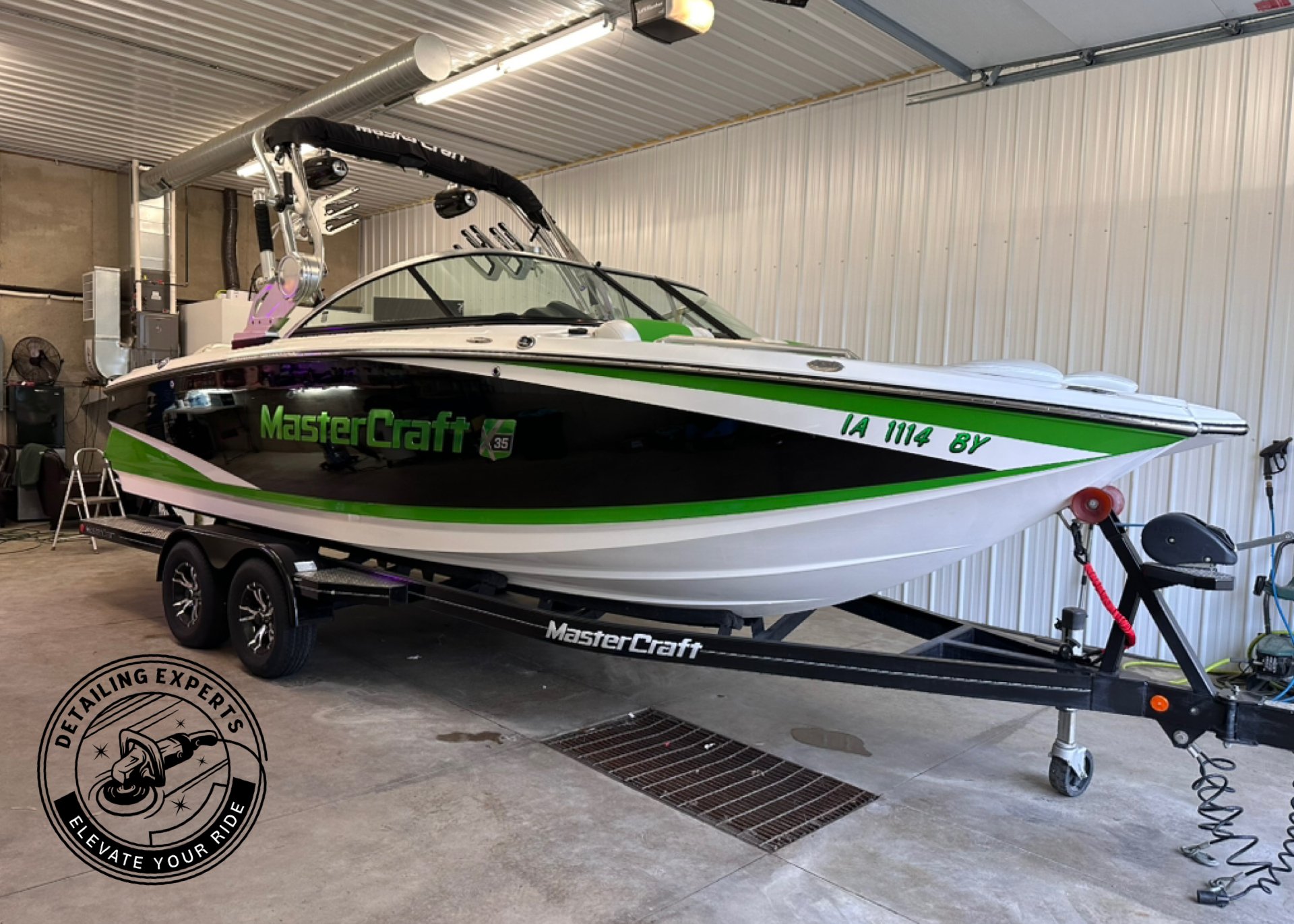 A black, white, and green MasterCraft speedboat on a black trailer inside a building or garage with concrete floor and metal walls.